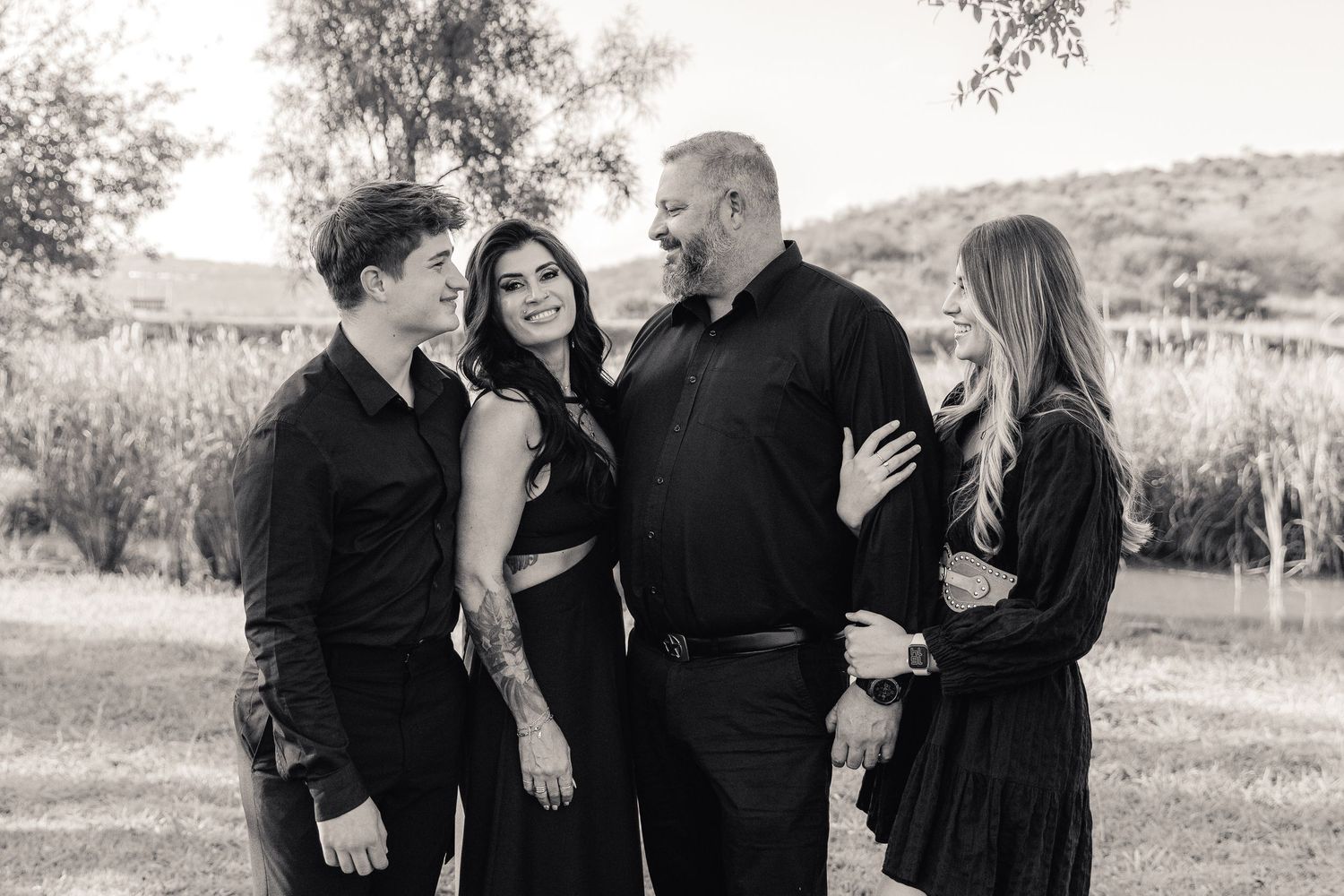 Black and white candid family photo of four people laughing together outdoors near a dam.