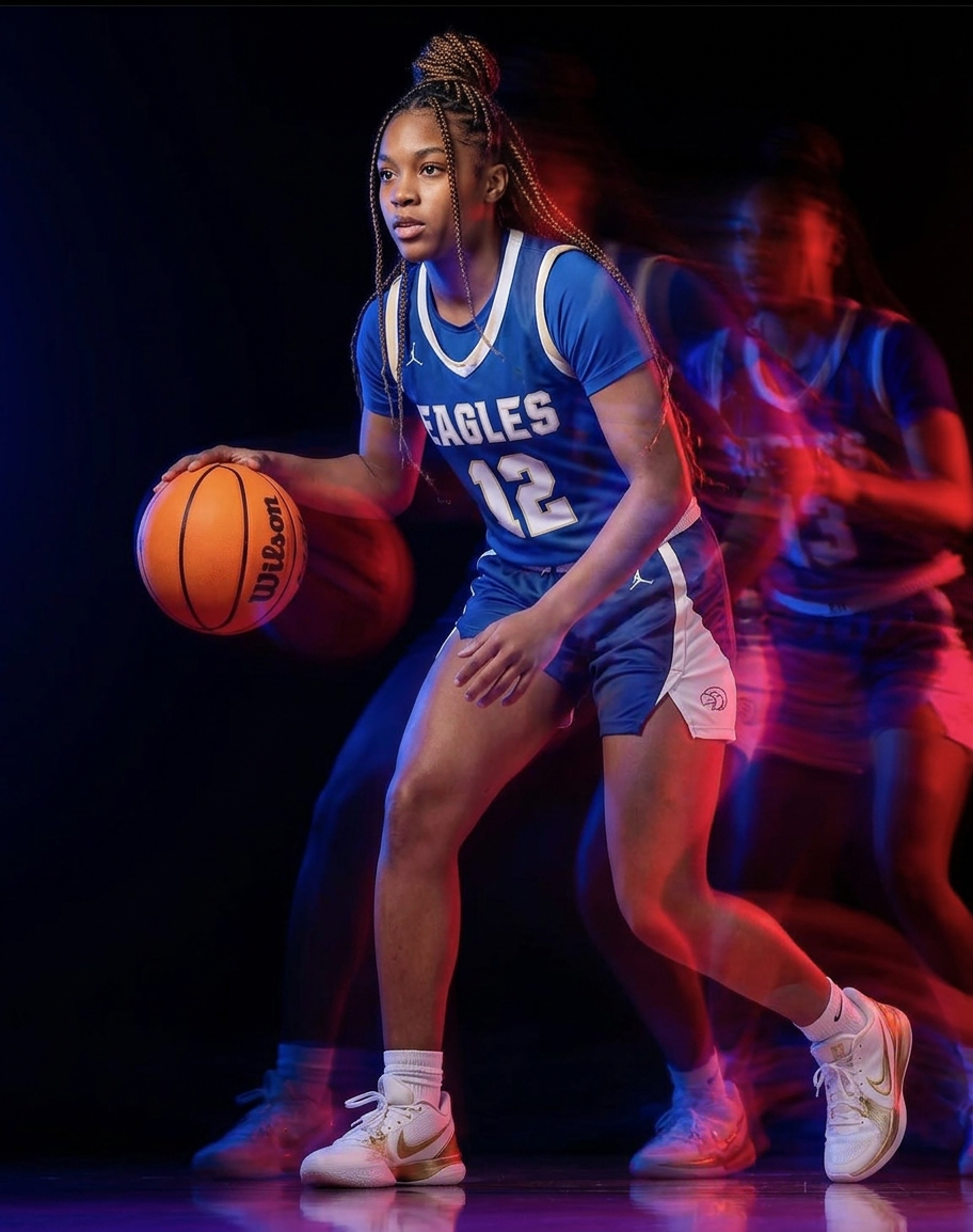 Female basketball player #12 in blue Eagles uniform dribbles ball in dramatic studio photo with motion blur effect.