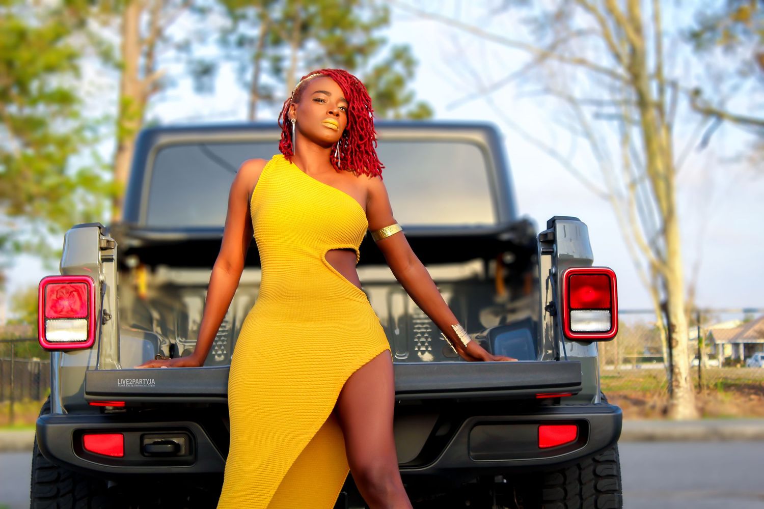 Woman in yellow cutout dress posing beside a dark SUV outdoors.