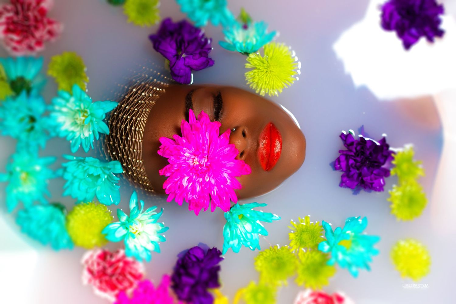 Woman surrounded by colorful flowers floating in a white milk bath.