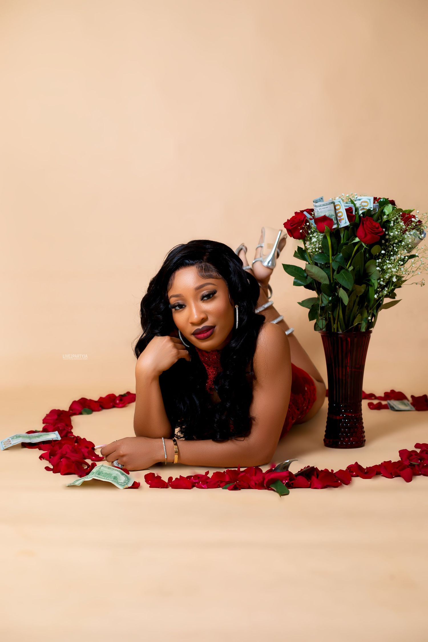 Woman in red outfit lying on floor beside red roses bouquet in heart-shaped petal arrangement.