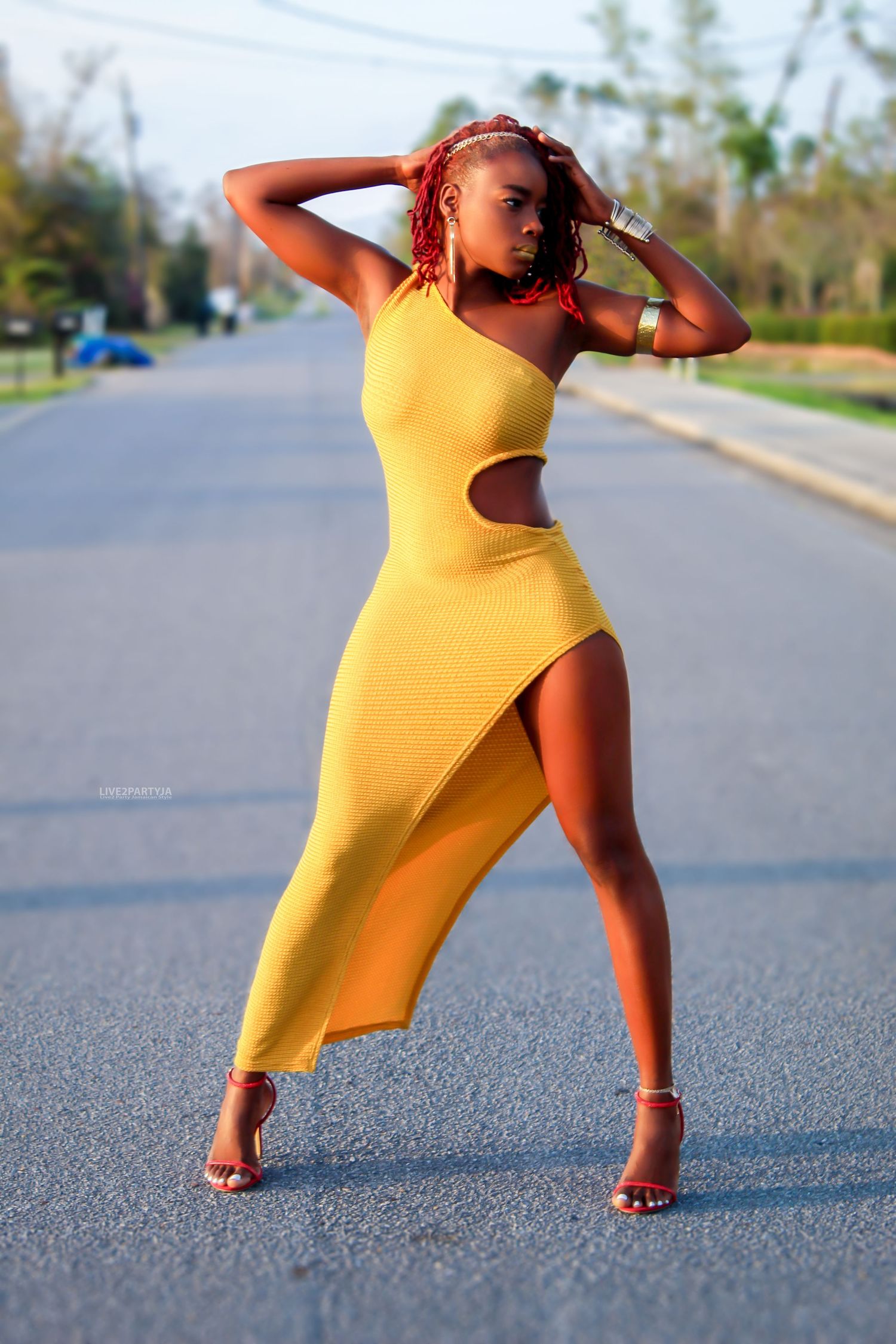 Woman in yellow asymmetric cutout dress posing confidently on an open road.