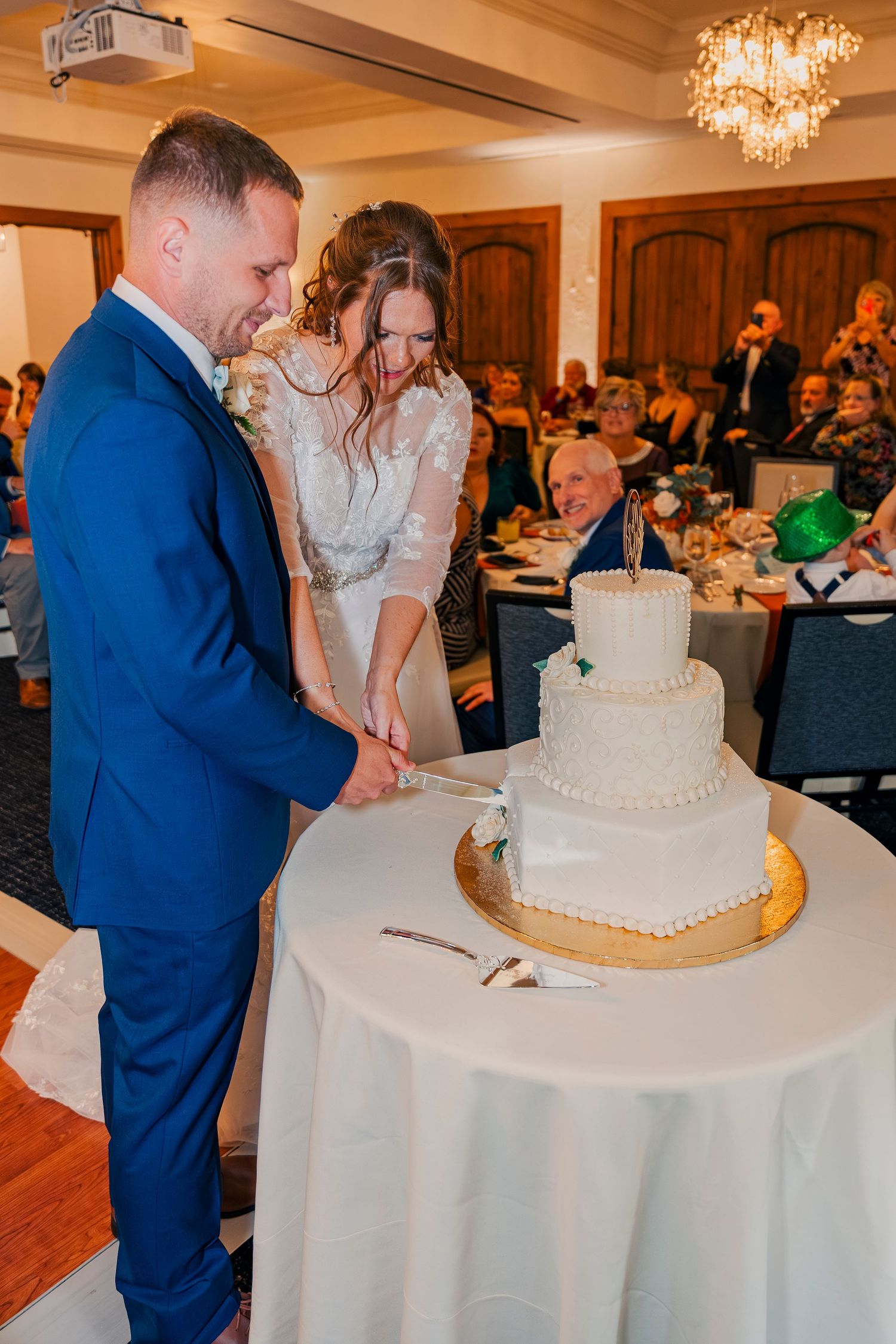 Bride and groom cutting their elegant three-tier white wedding cake at a vineyard reception.