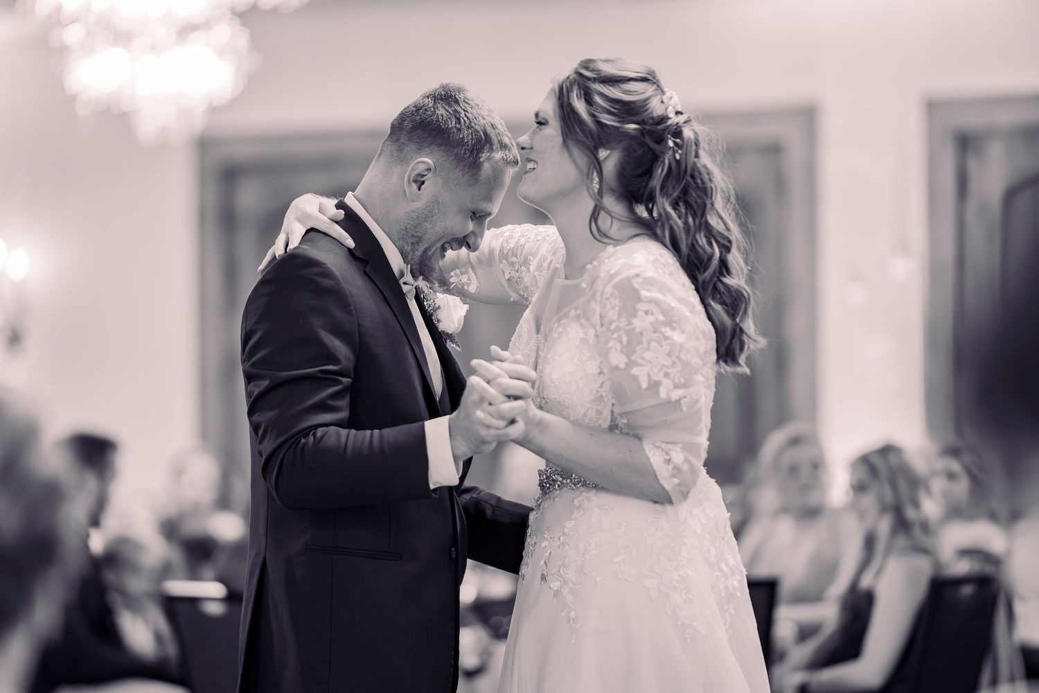 Bride and groom share an intimate moment during their first dance at wedding reception in black and white.