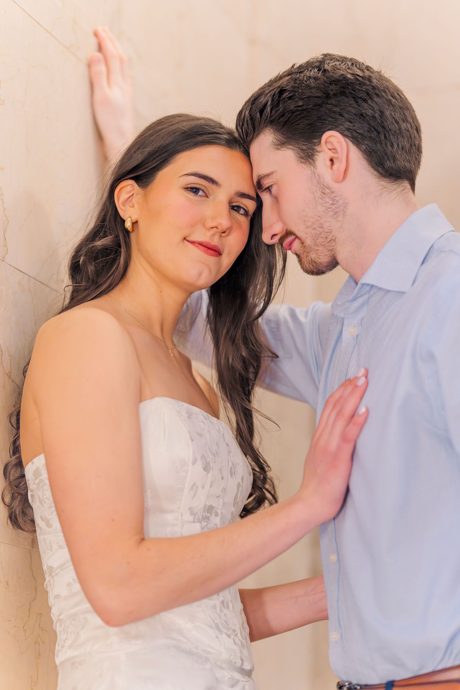 A couple share an intimate moment, leaning foreheads together against a beige wall. Engagement photo session at the Cleveland Public Library