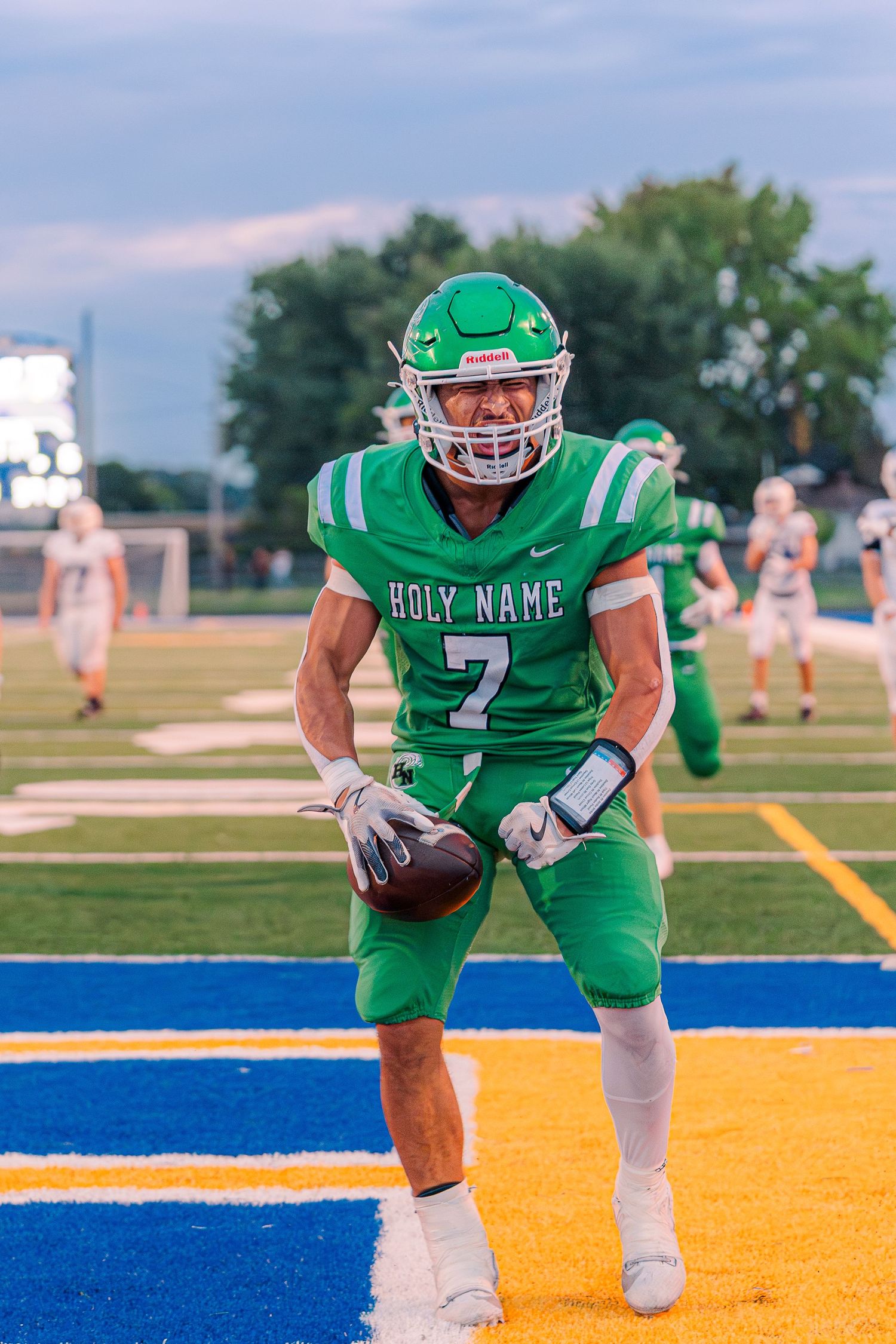 Holy Name #7 football player celebrates in the end zone holding the ball during a high school game.