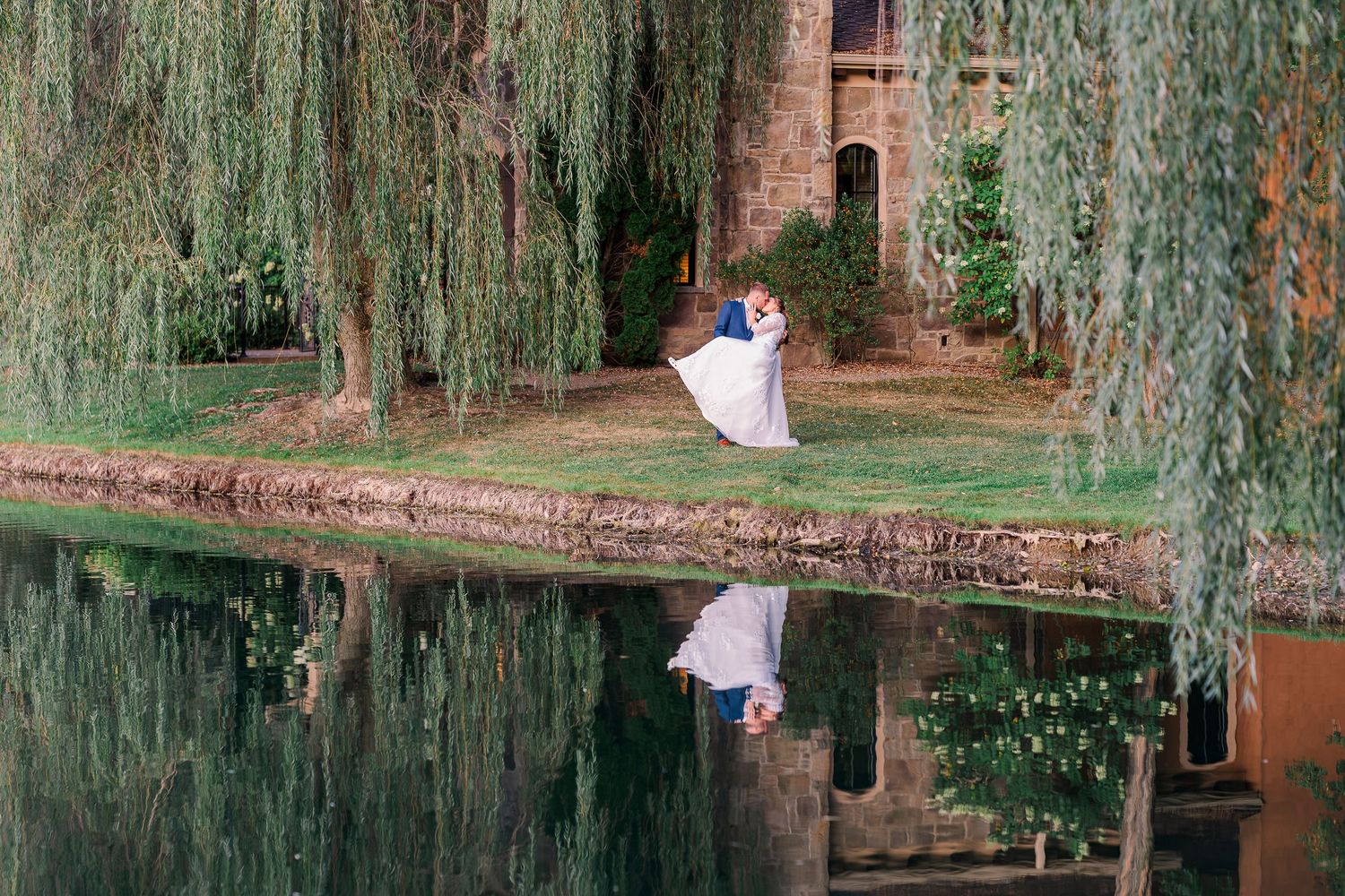 Bride and groom dancing near pond under weeping willow trees at Gervasi Vineyard wedding venue.