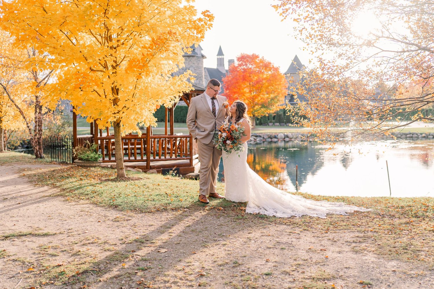 Bride and groom walk hand in hand near a pond surrounded by vibrant autumn foliage at Castle Farms in Charlevoix, Michigan