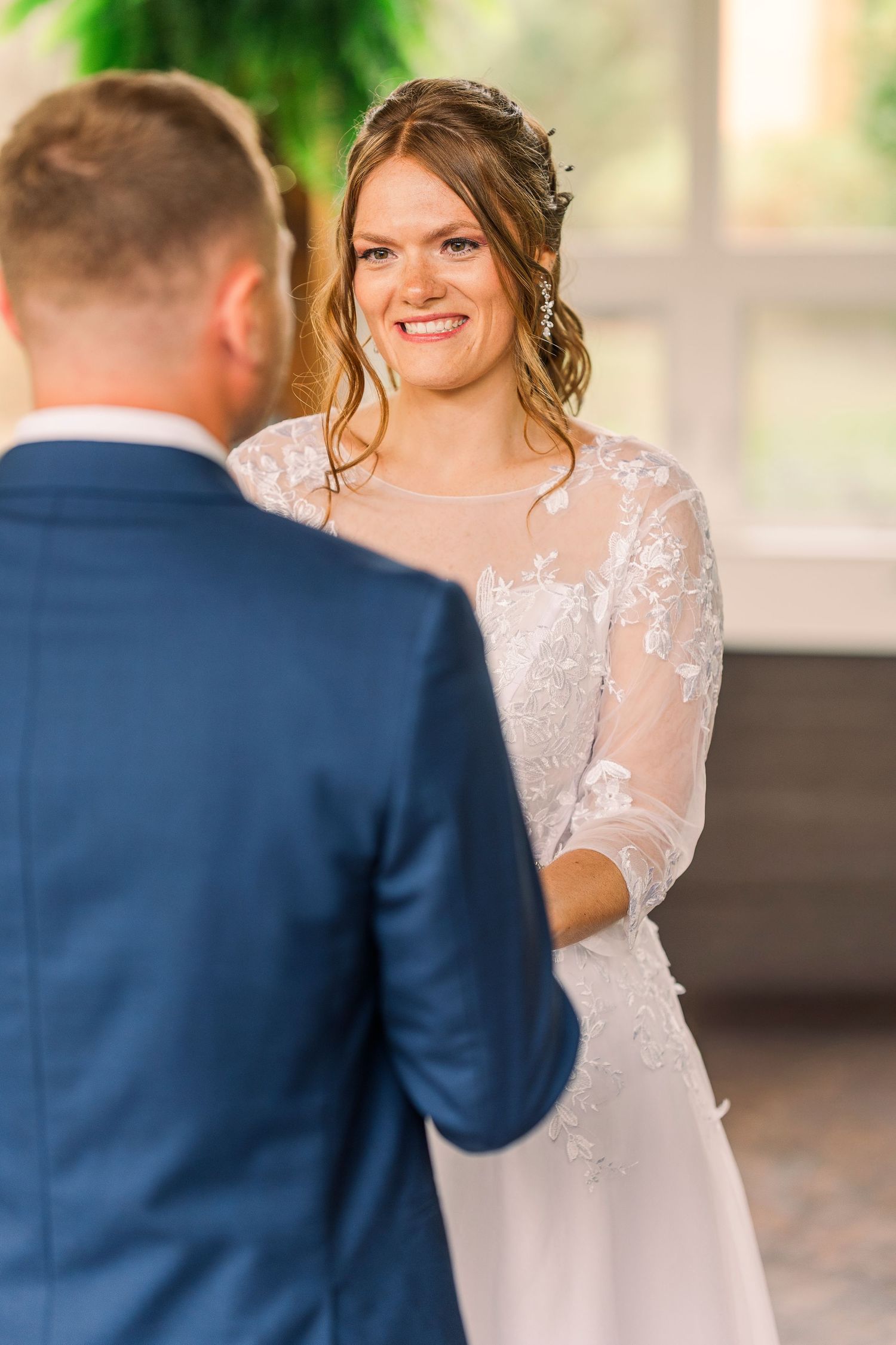 Smiling bride in lace wedding dress holding hands with groom at wedding ceremony.