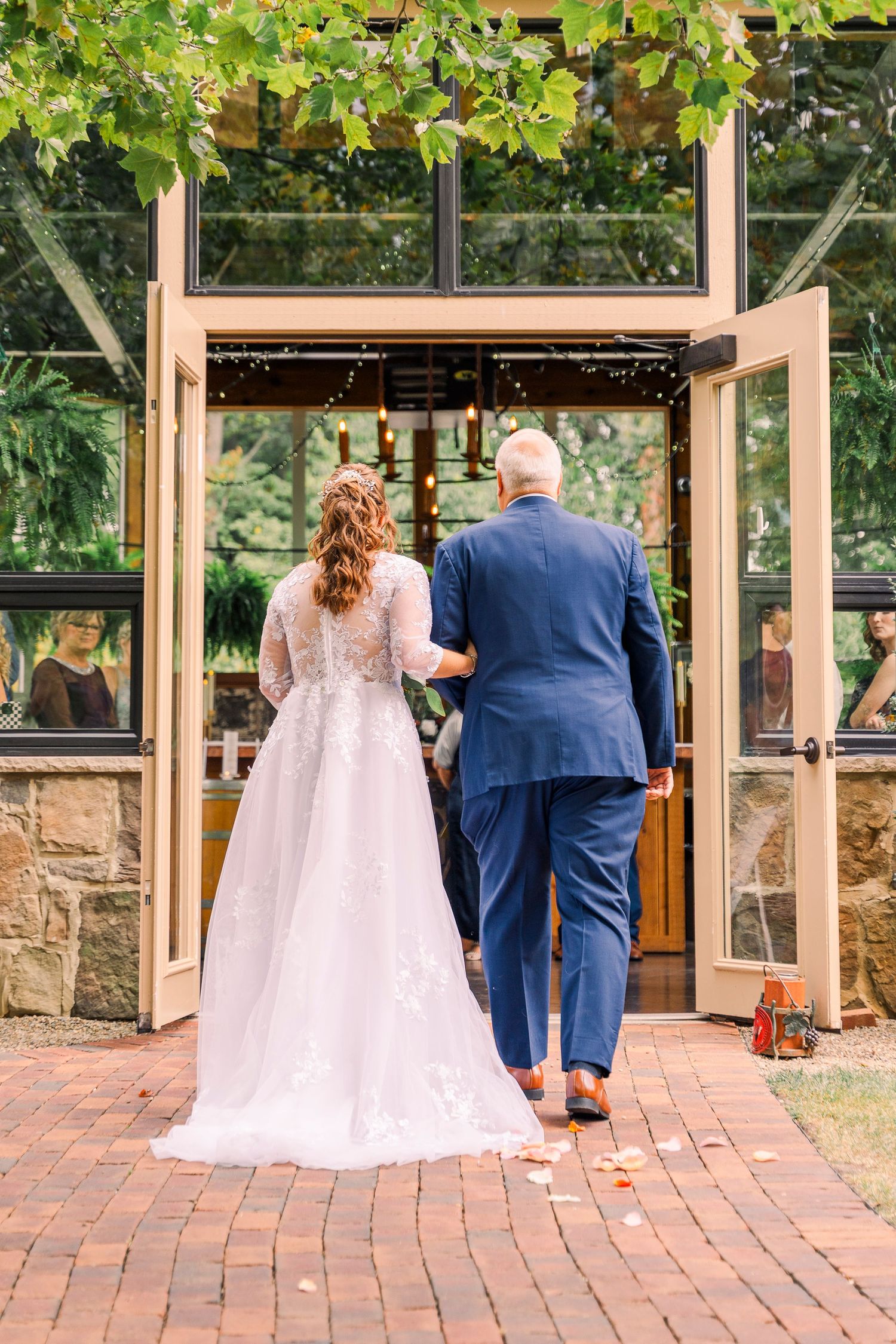 Bride in lace gown and escort in navy suit enter the conservatory at Gervasi Vineyard wedding venue from behind.