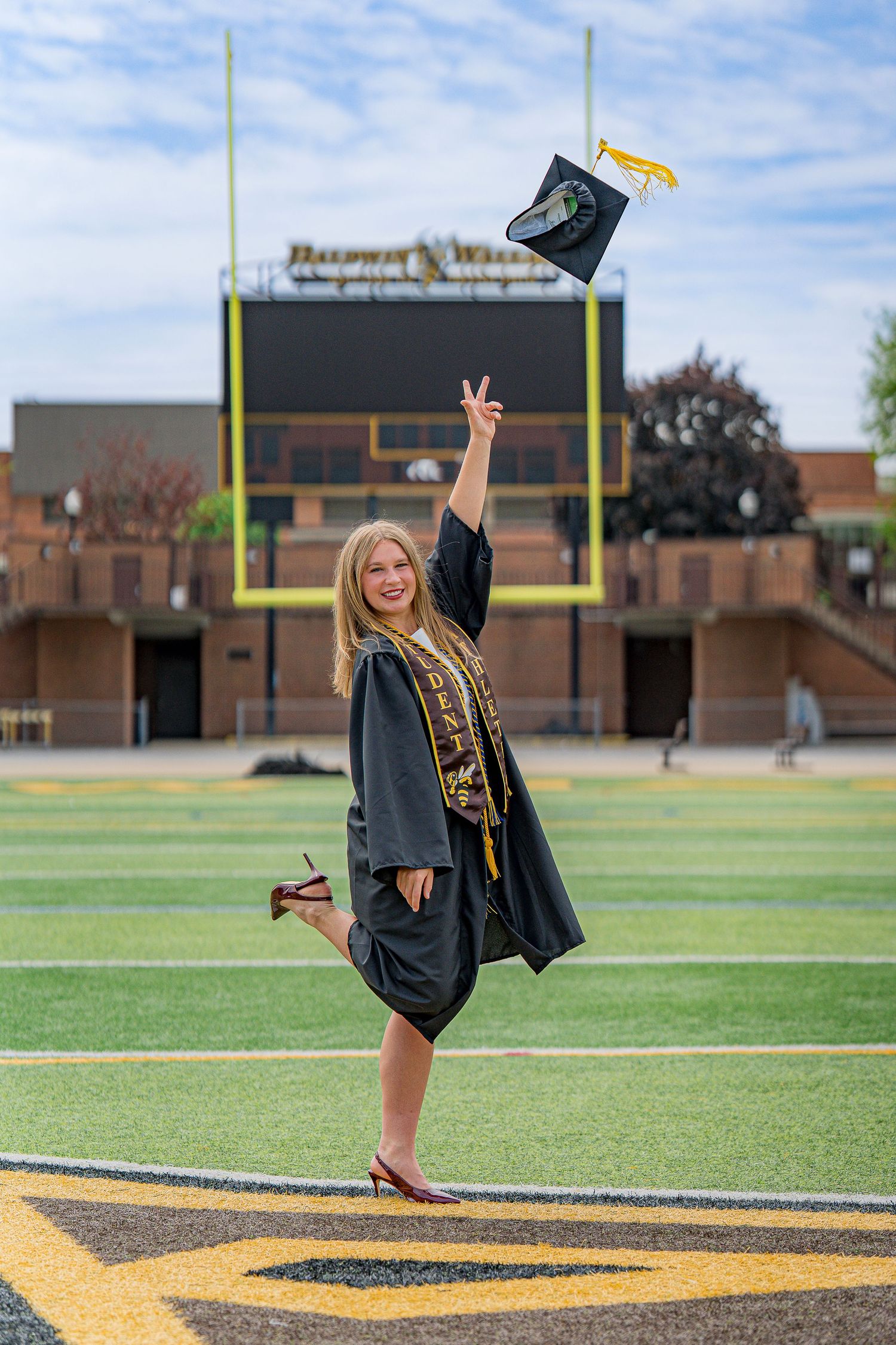A graduating woman in cap and gown tosses her cap in the air on a college football field at Baldwin Wallace University in Berea, Ohio