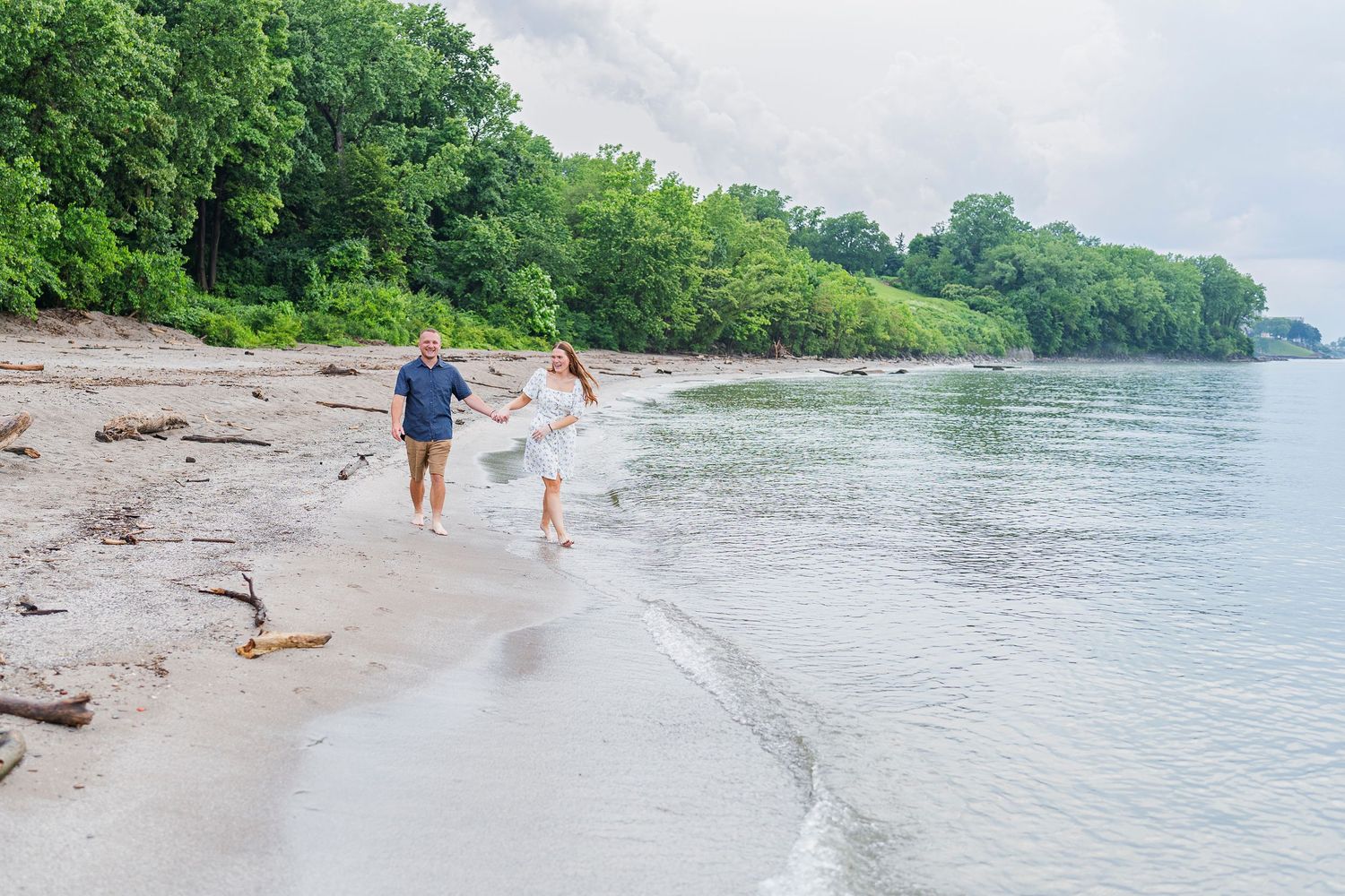 A couple walks hand in hand along a lush green shoreline on a cloudy day at Edgewater Park in Cleveland, Ohio