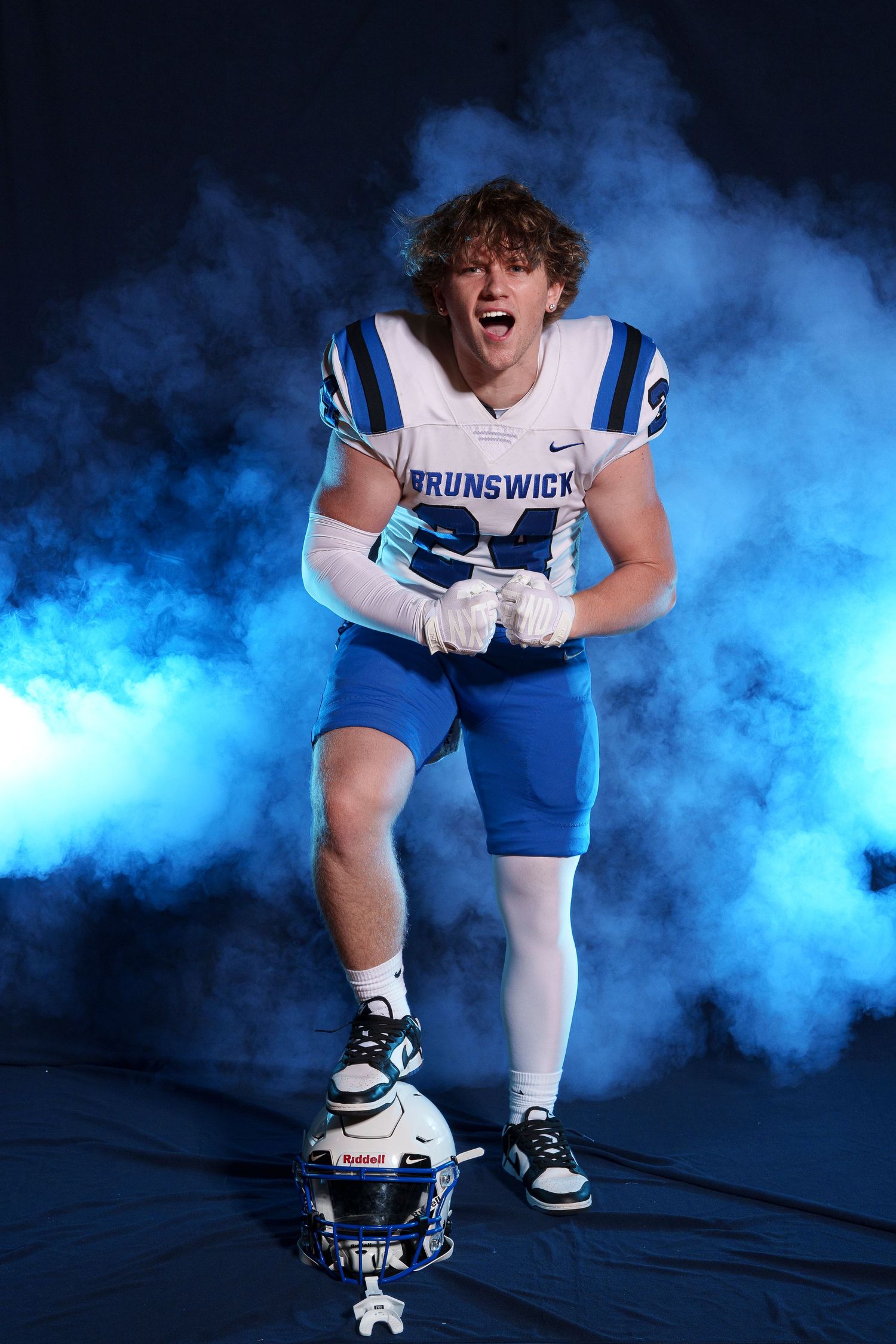 Brunswick football player number 24 posing with helmet in dramatic blue smoke.
