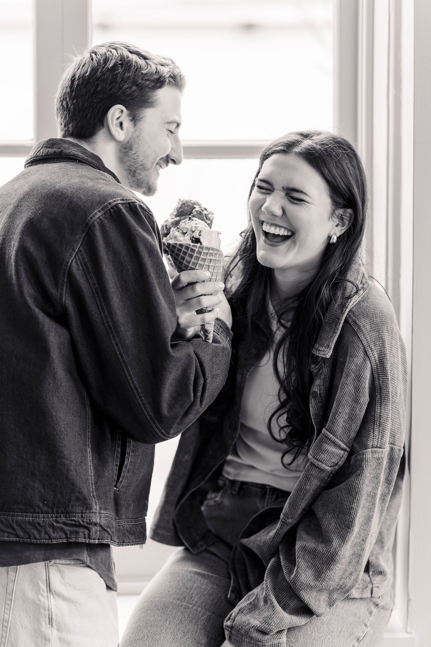 A laughing couple shares an ice cream cone in a black and white photo near a bright window at Mitchell's Ice cream in Cleveland Ohio
