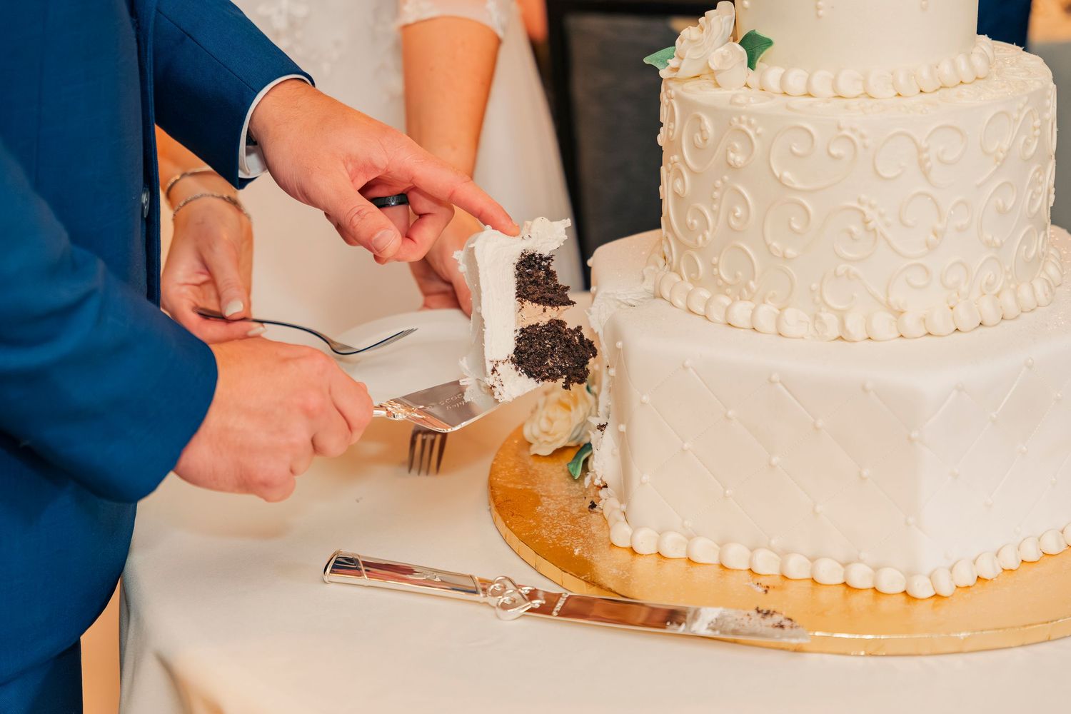 Close-up of bride and groom cutting a three-tier white wedding cake revealing Oreo filling.