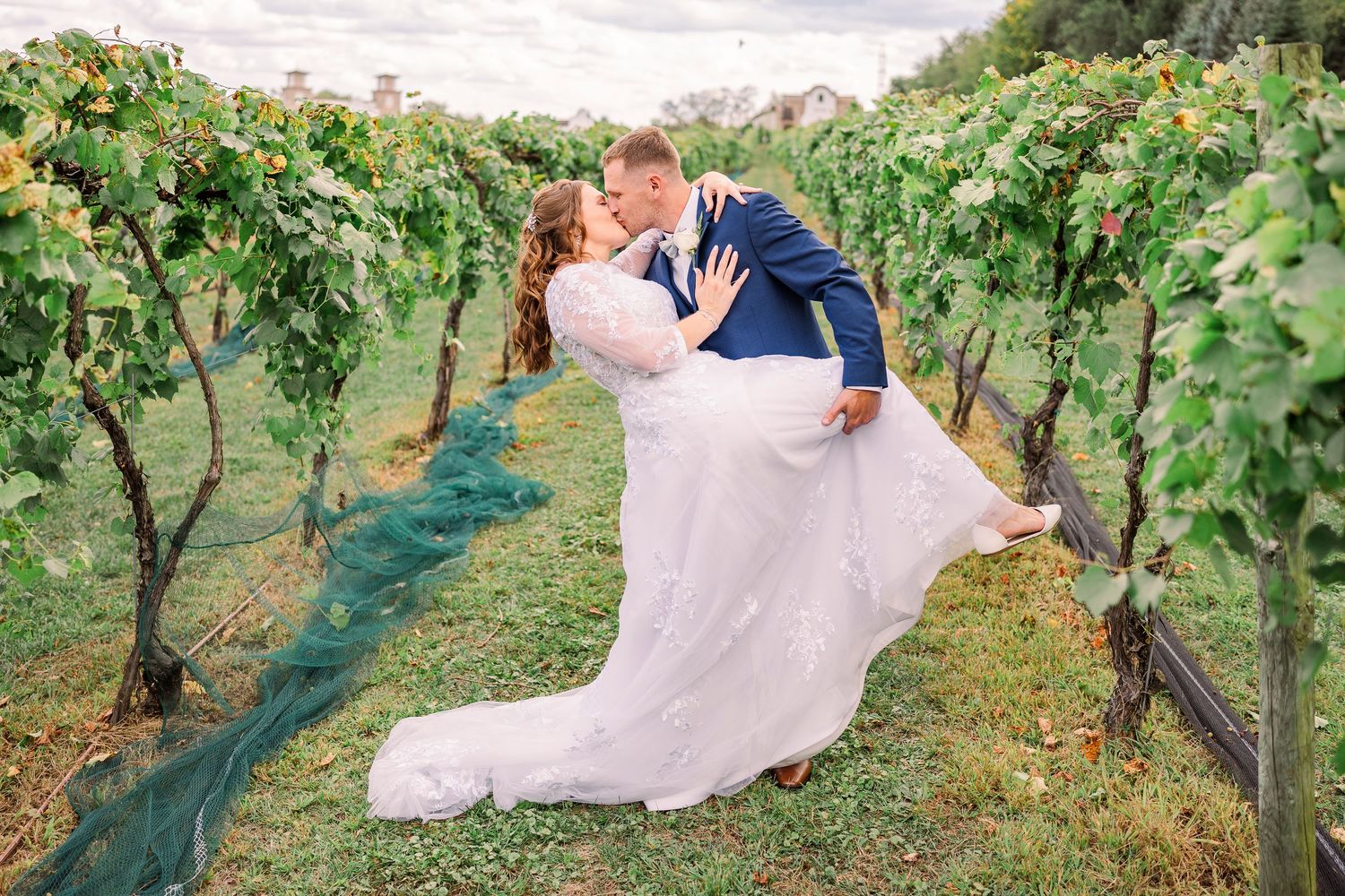 Groom dipping bride for a romantic kiss among lush green vineyard rows at Gervasi