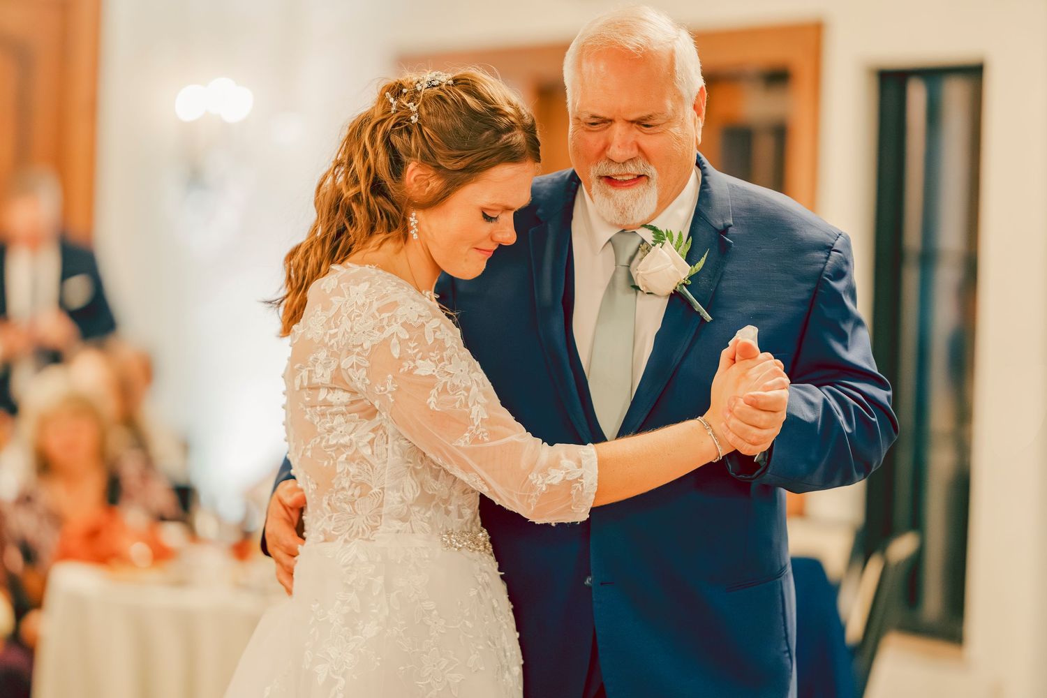 Bride shares emotional father-daughter dance in lace wedding gown at wedding reception.
