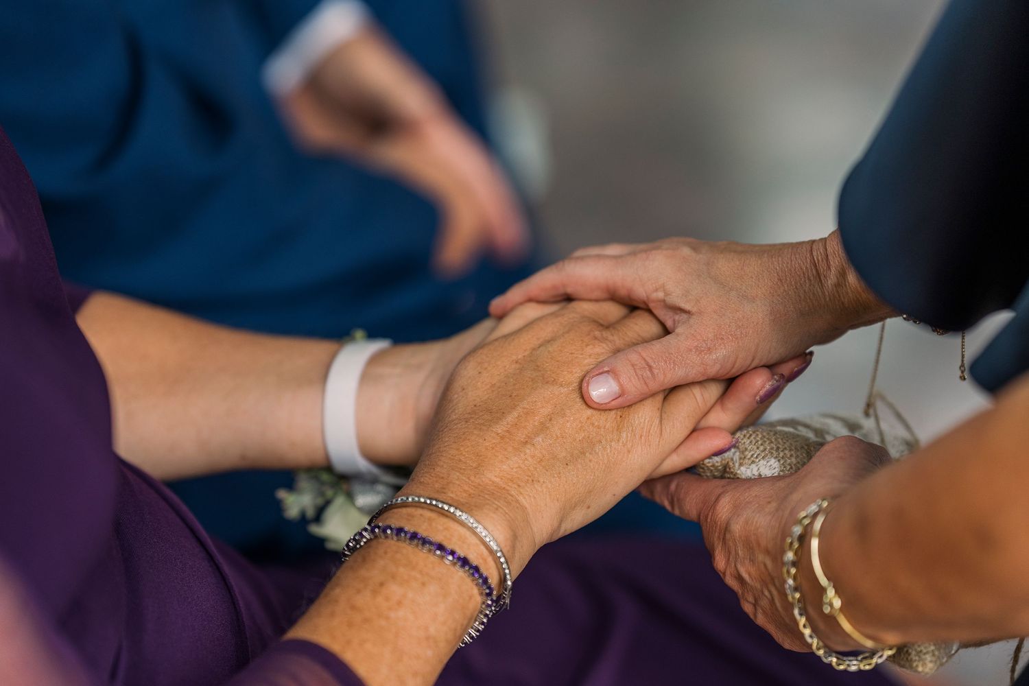 Close-up of hands gently held together with bracelets at a wedding ceremony.