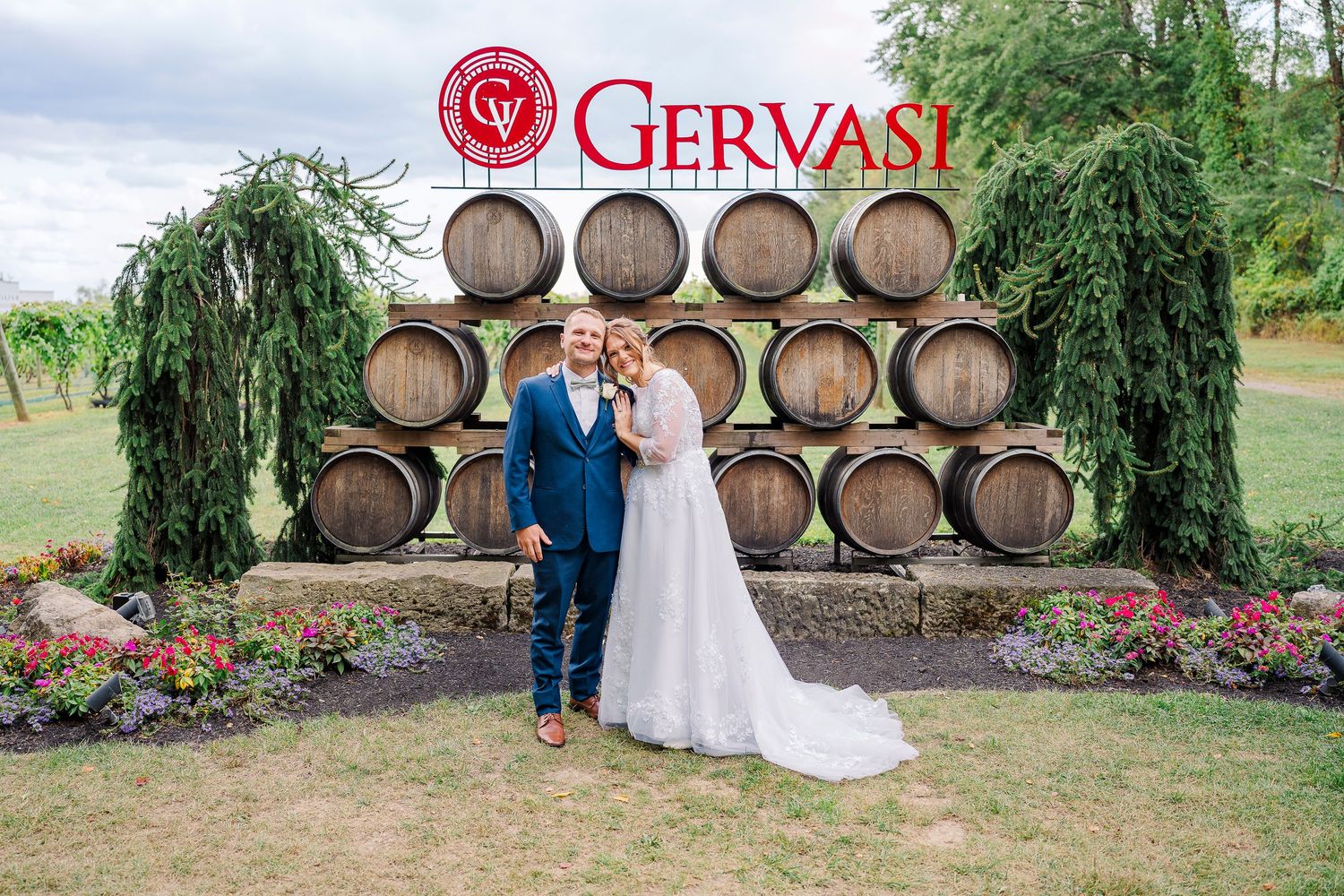Smiling couple posing in front of wine barrel display at Gervasi Vineyard wedding venue.