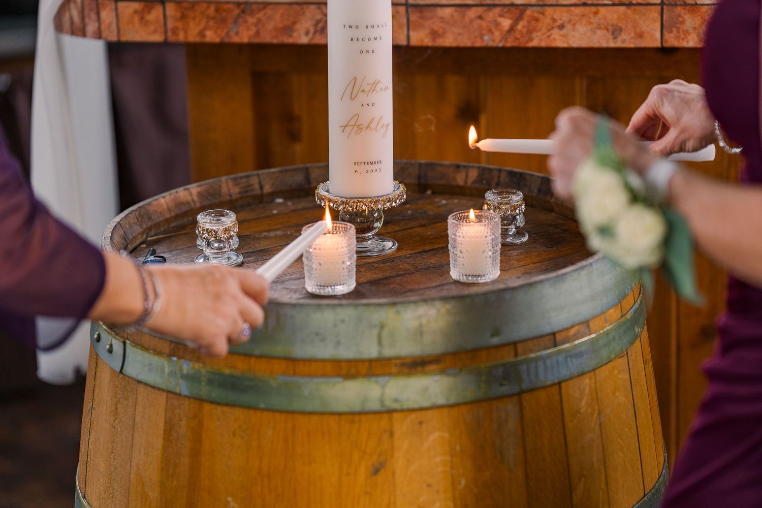 Hands lighting candles on a rustic wooden barrel during a wedding unity candle ceremony.