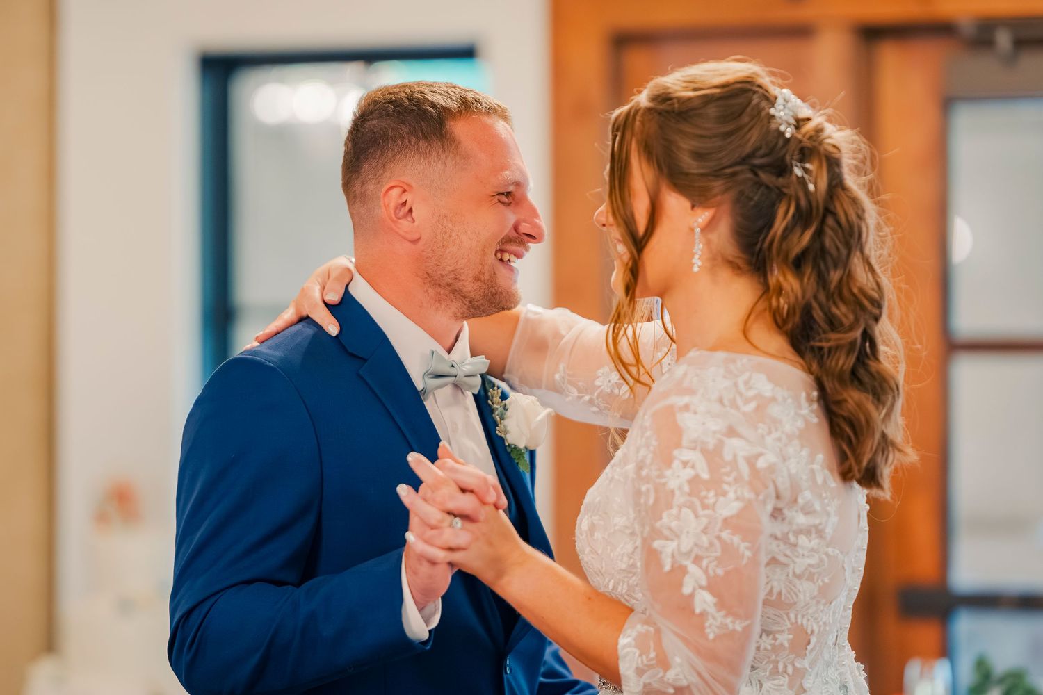 Bride and groom share a joyful first dance, smiling at each other in elegant wedding attire.