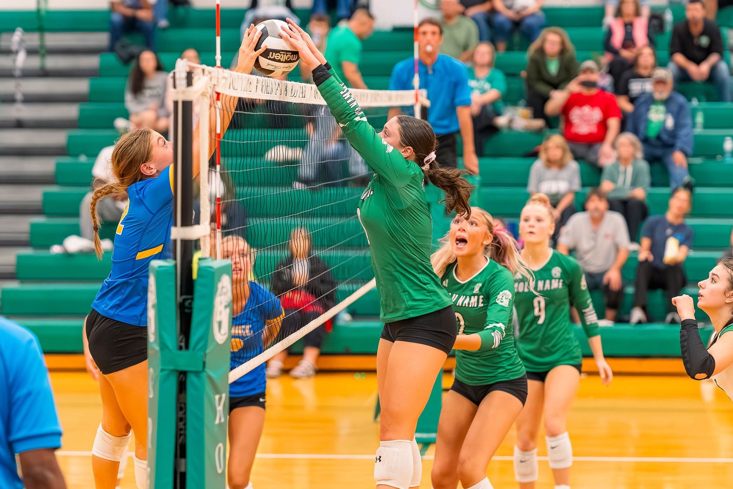 Holy Name High school girls volleyball player blocking ball at net during competitive match.