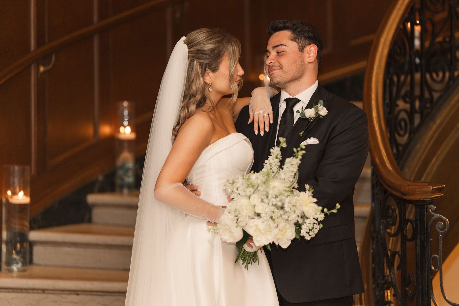 Bride and groom share a romantic moment on elegant staircase at the Columbus Athletic Club. Bride wear white lacy dress and veil