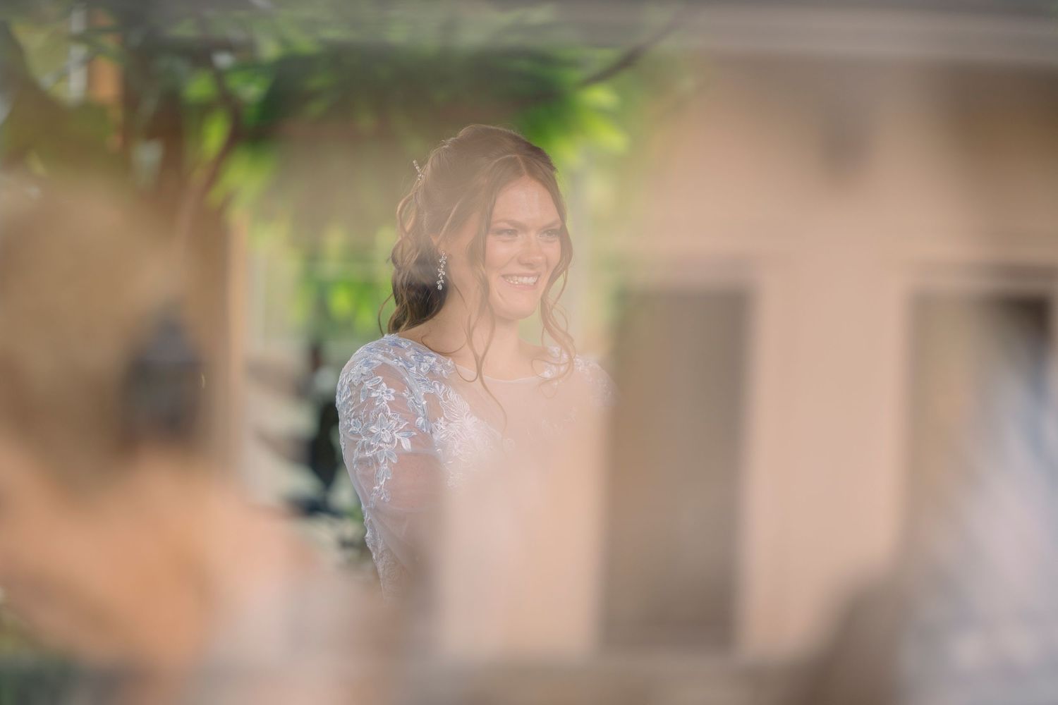 Radiant bride in lace wedding gown smiling joyfully during outdoor wedding ceremony.