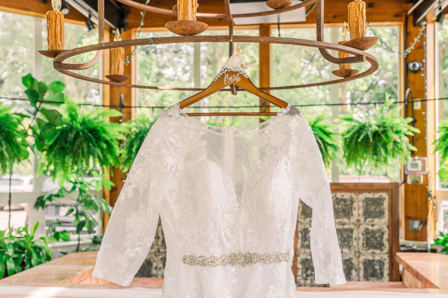 Long-sleeve lace wedding gown hanging on wooden hanger in the conservatory at Gervasi Vineyard wedding venue.