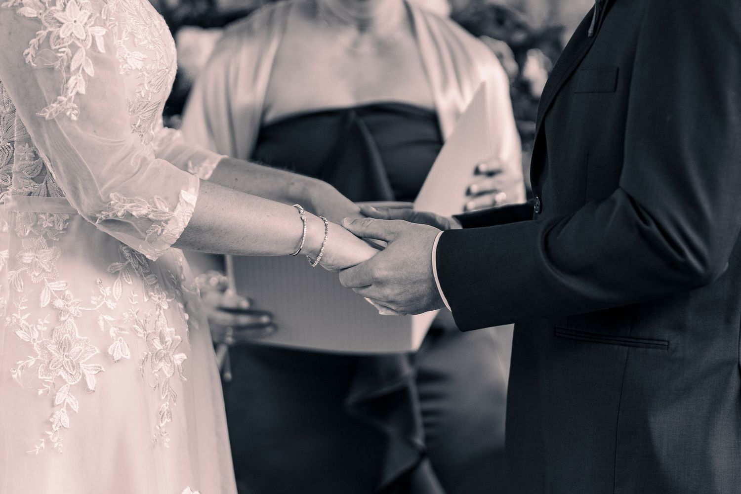Black and white photo of bride and groom holding hands during wedding ceremony.