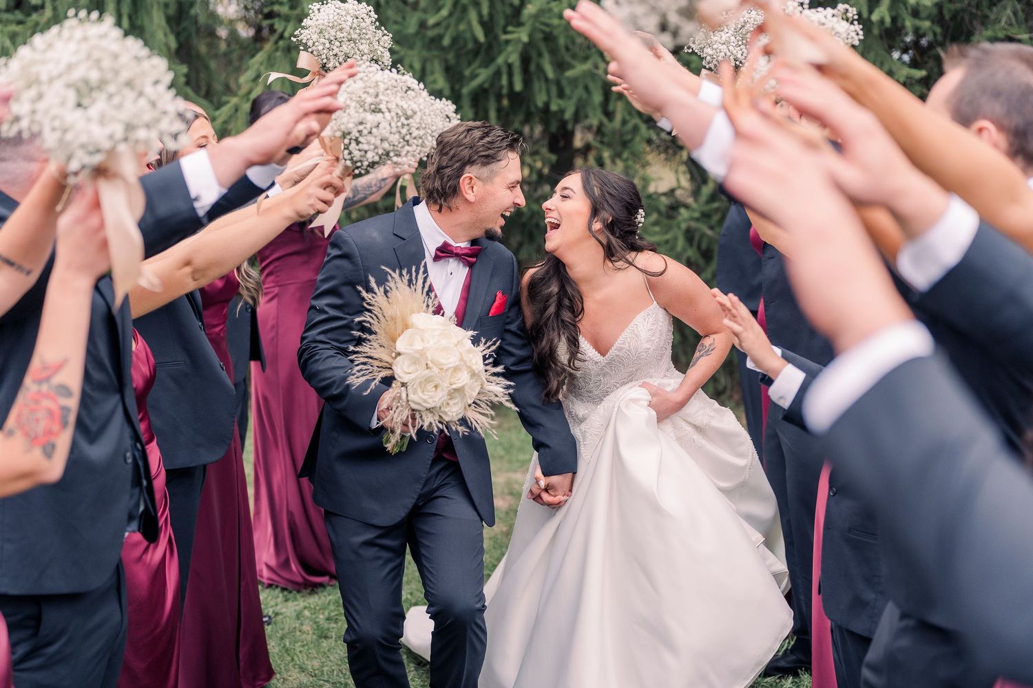 Bride and groom laughing as wedding party tosses dried flowers during celebratory outdoor sendoff.
