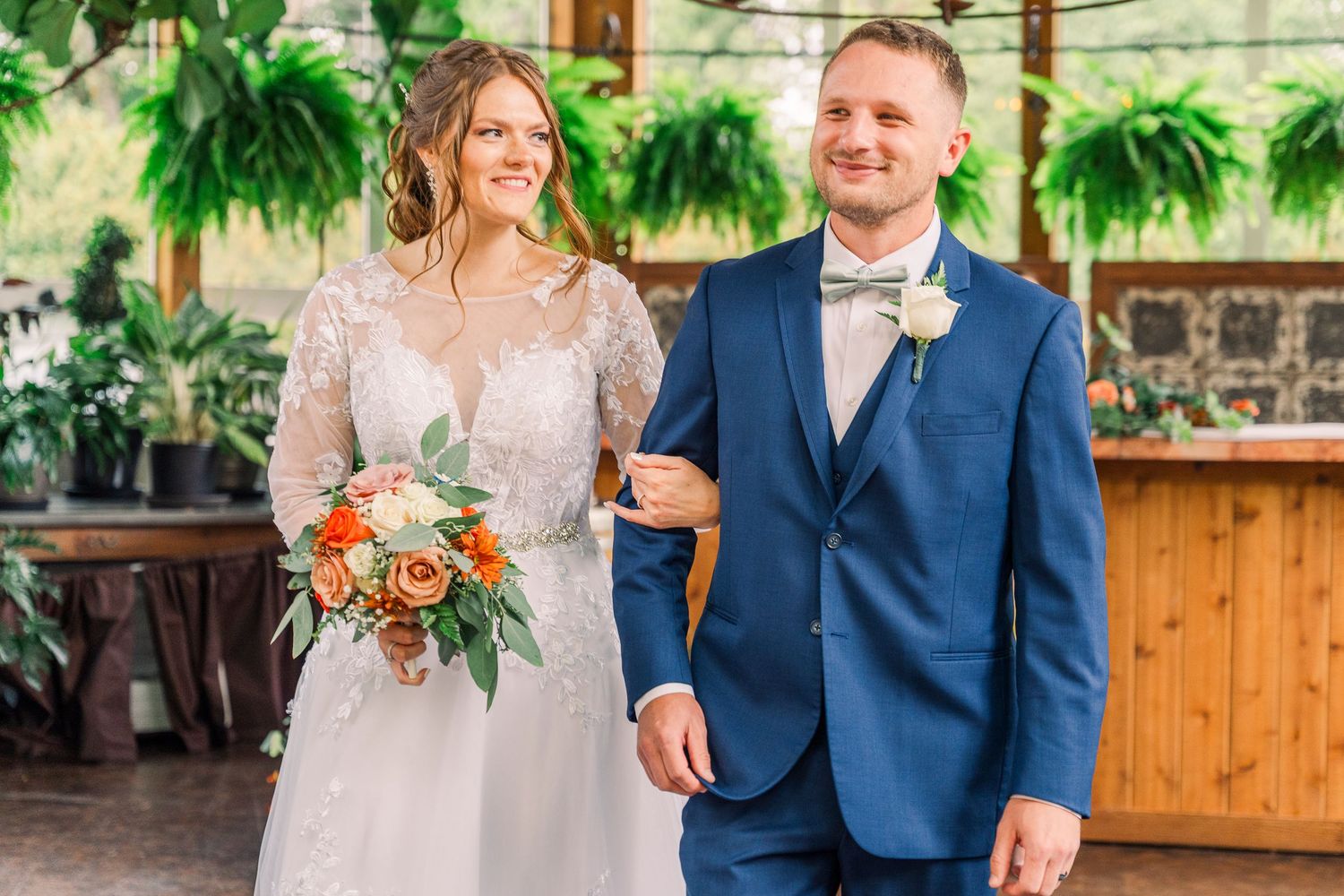 Smiling bride and groom walking together, bride holding a bouquet of flowers in the conservatory at Gervasi Vineyard wedding venue.