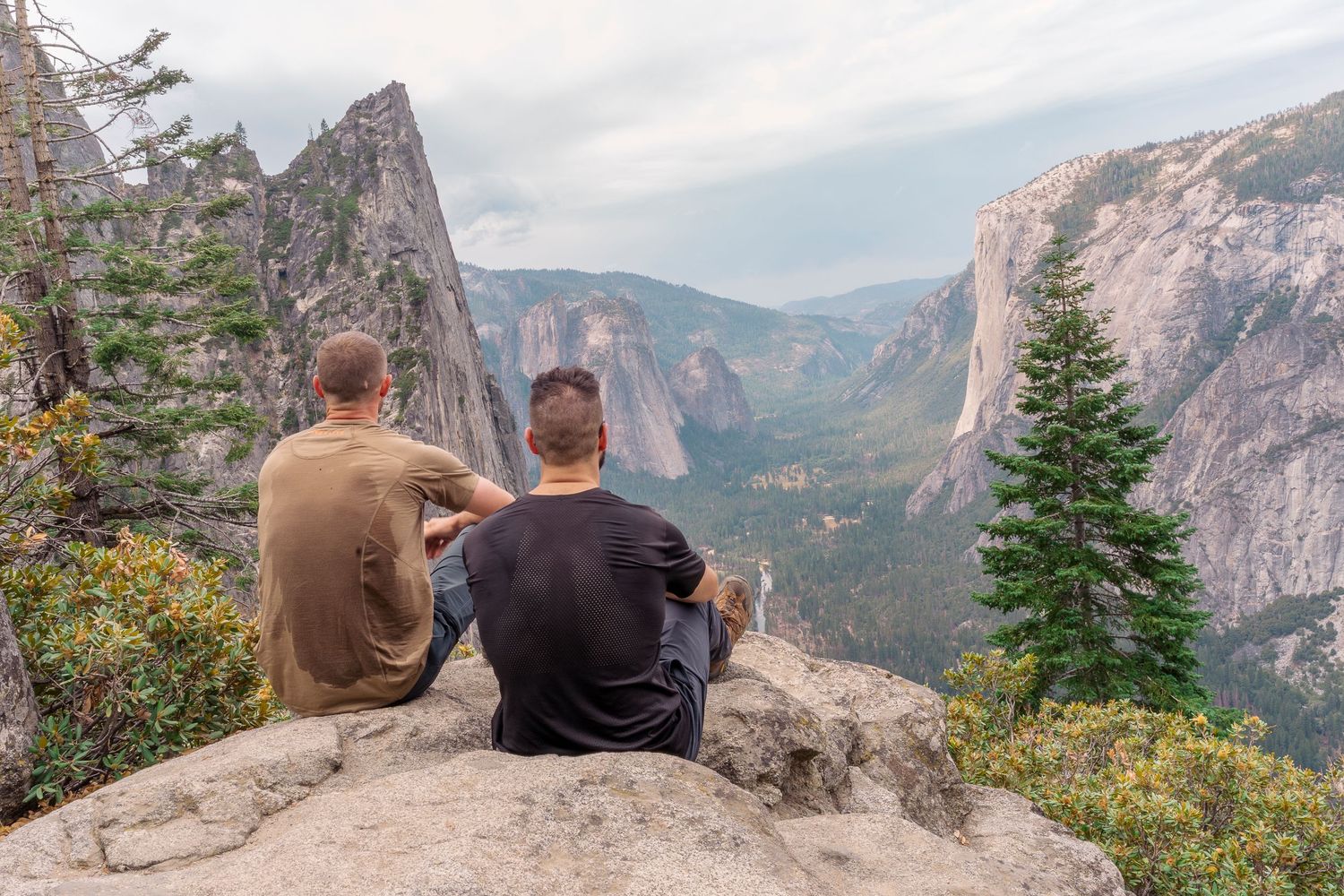 Two friends sitting on a mountain rock overlooking a stunning Yosemite Valley landscape.