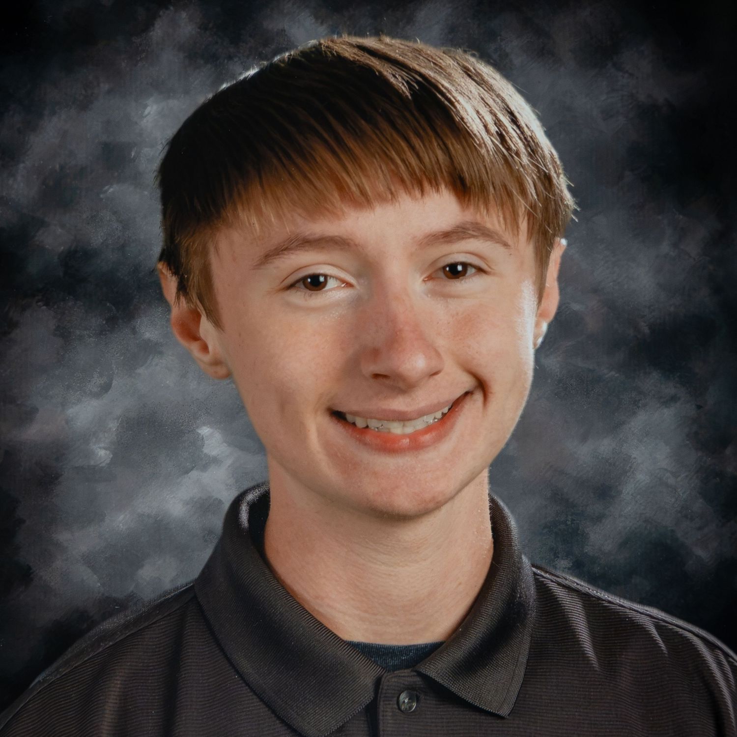 A smiling teenage boy with brown hair and braces poses for a school portrait against a dark gray studio background.