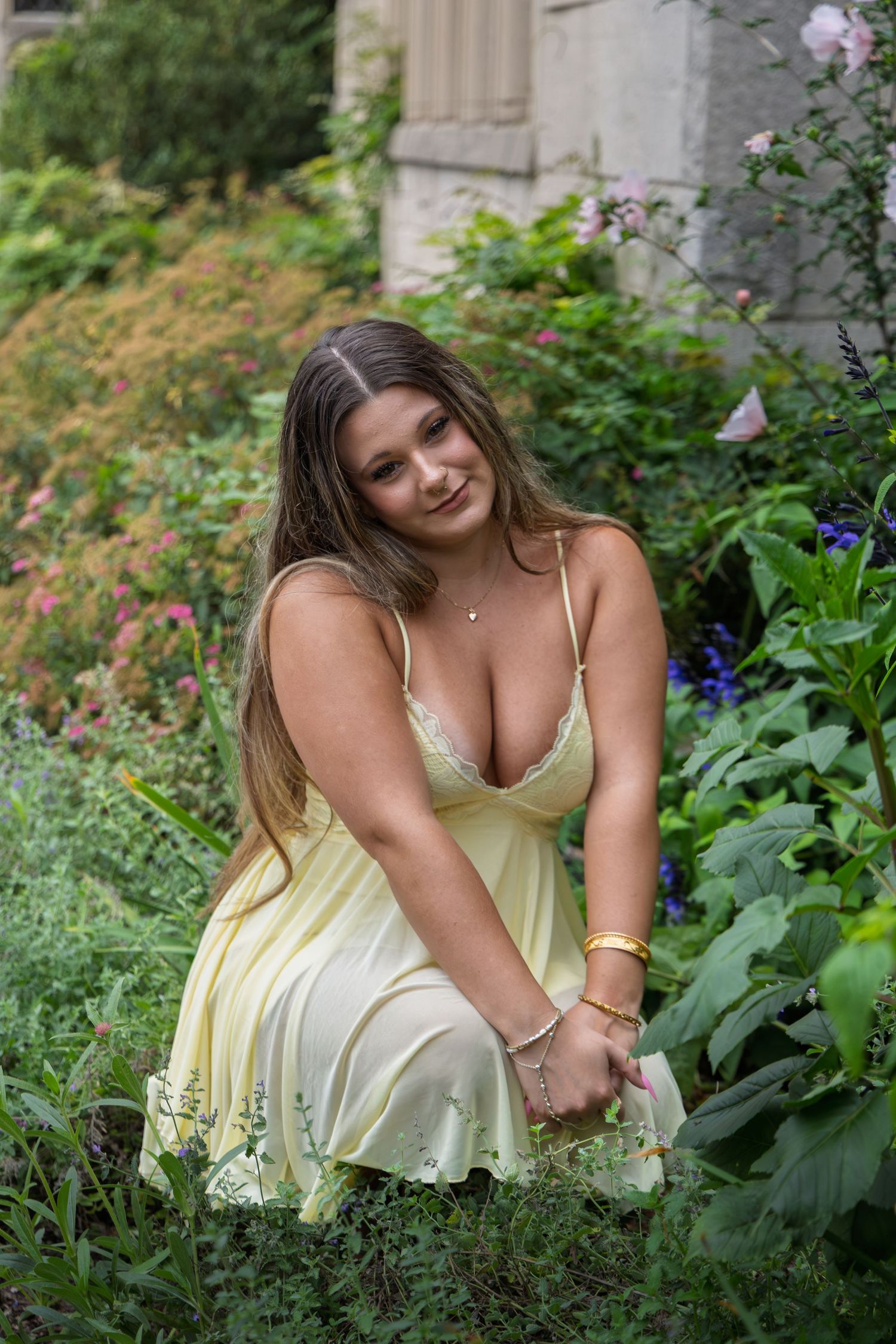 Young woman in yellow sundress crouching in a lush garden surrounded by colorful flowers.