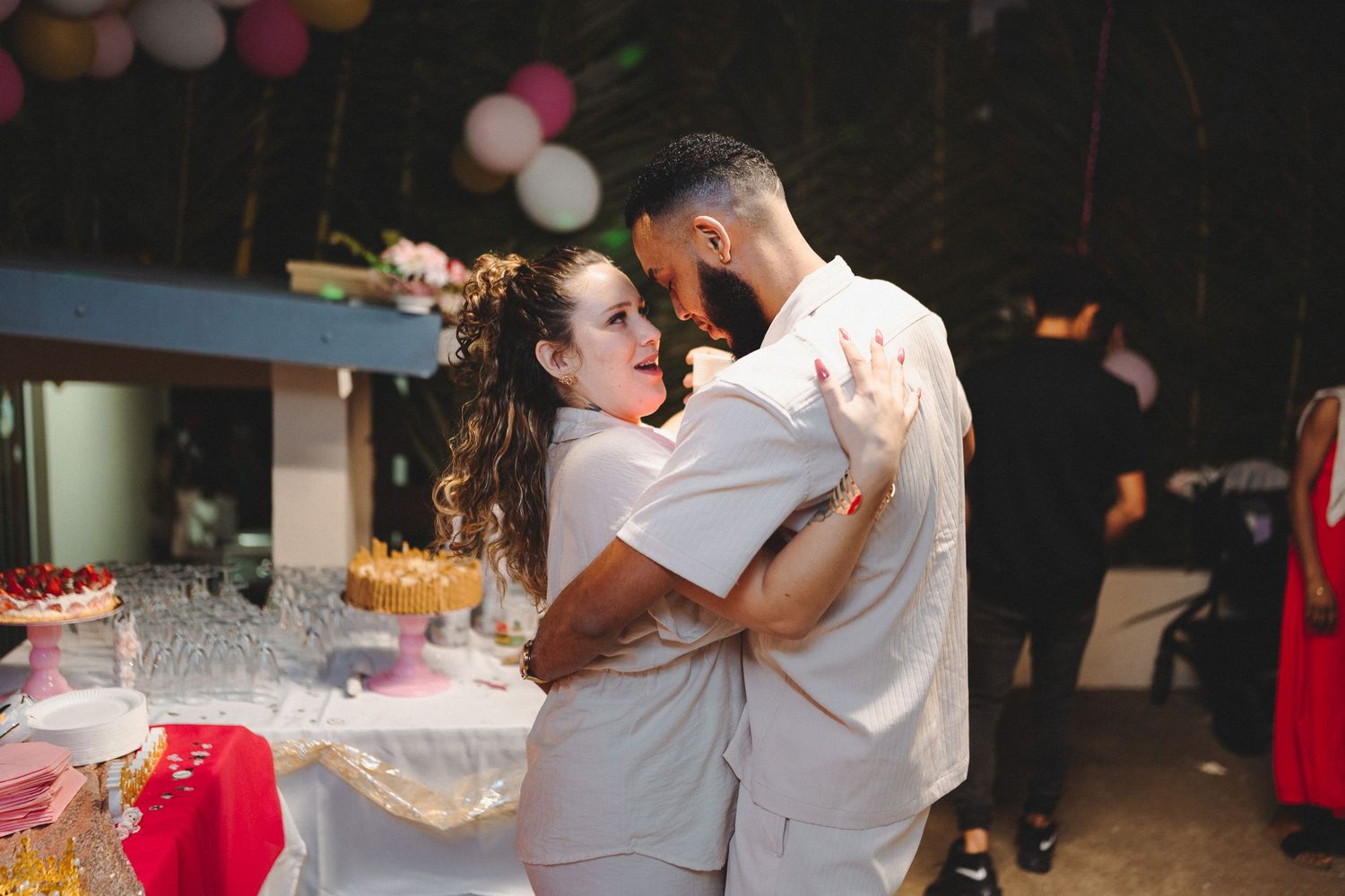 Couple shares first dance at outdoor wedding reception with colorful balloon decorations and dessert table in background.