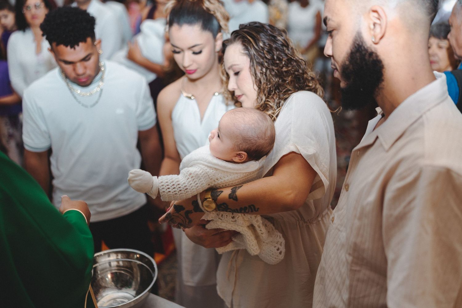 A mother holds her baby during a baptism ceremony with godparents standing nearby at a church font.