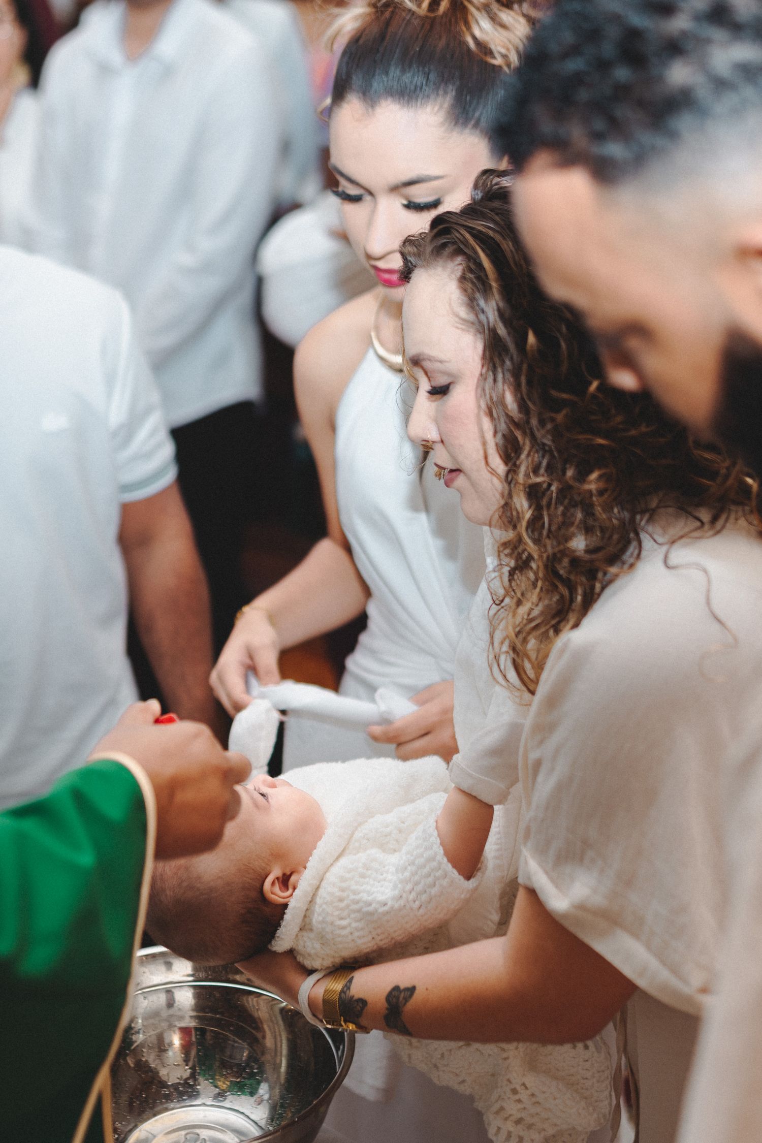 A priest baptizes a newborn baby held by a woman in white during a religious christening ceremony.