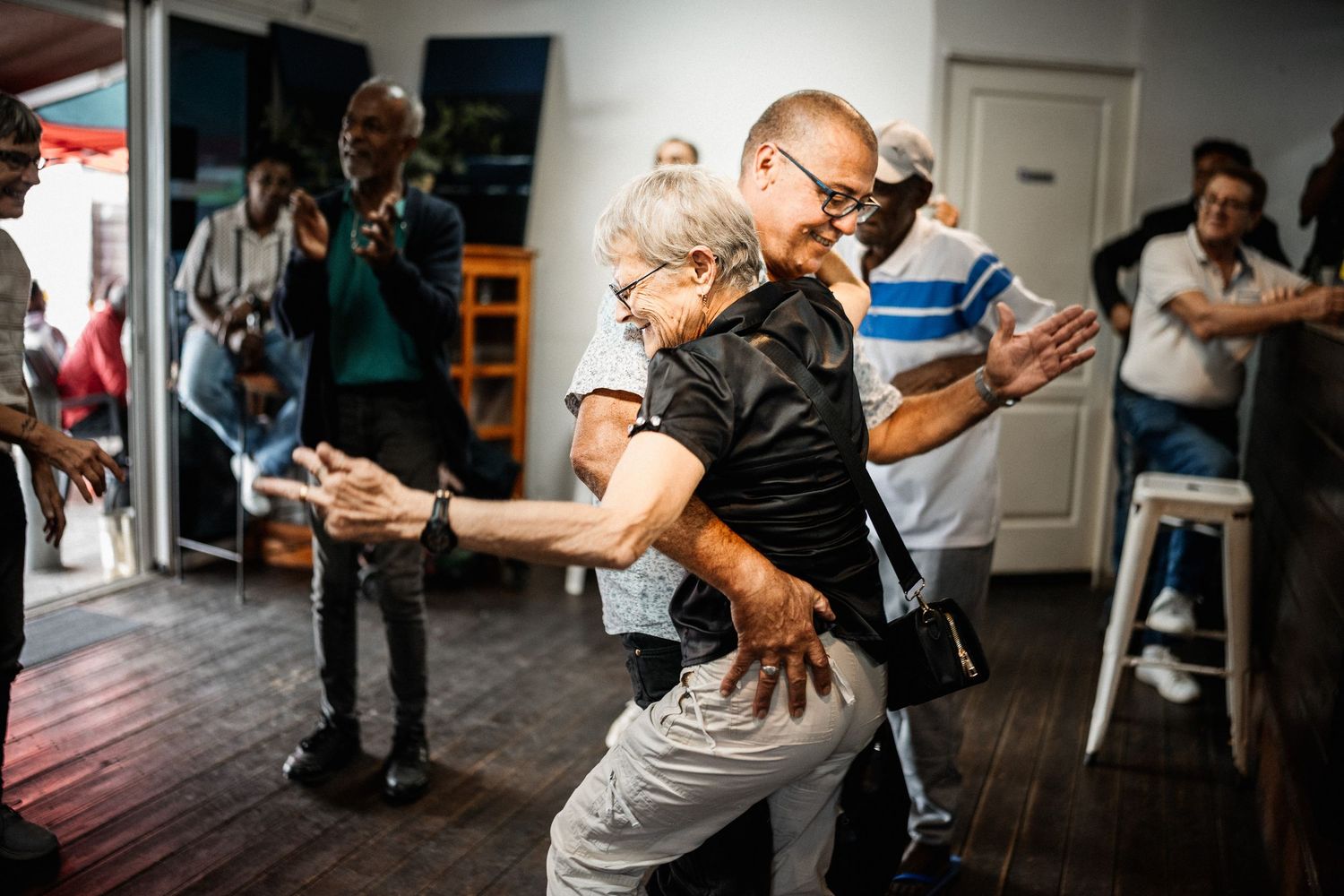 Energetic elderly couple dancing together at lively indoor social event with crowd watching.