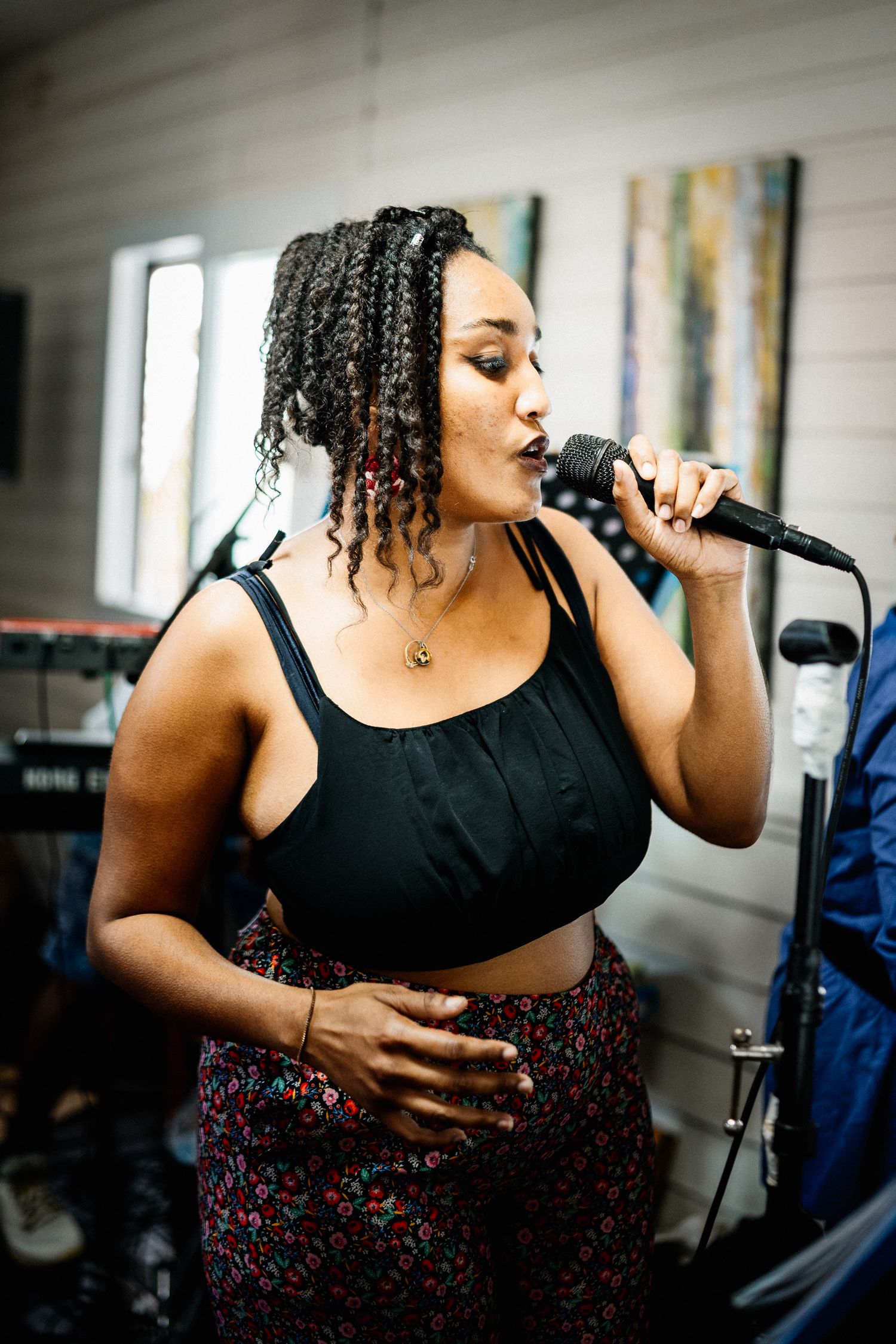 Young woman with braided hair singing passionately into a microphone at an indoor music event.