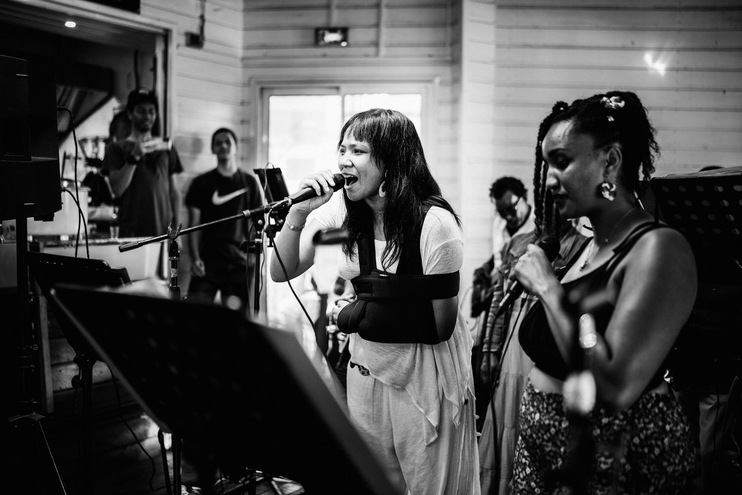 Black and white photo of two women singing into microphones on stage at a live music performance.