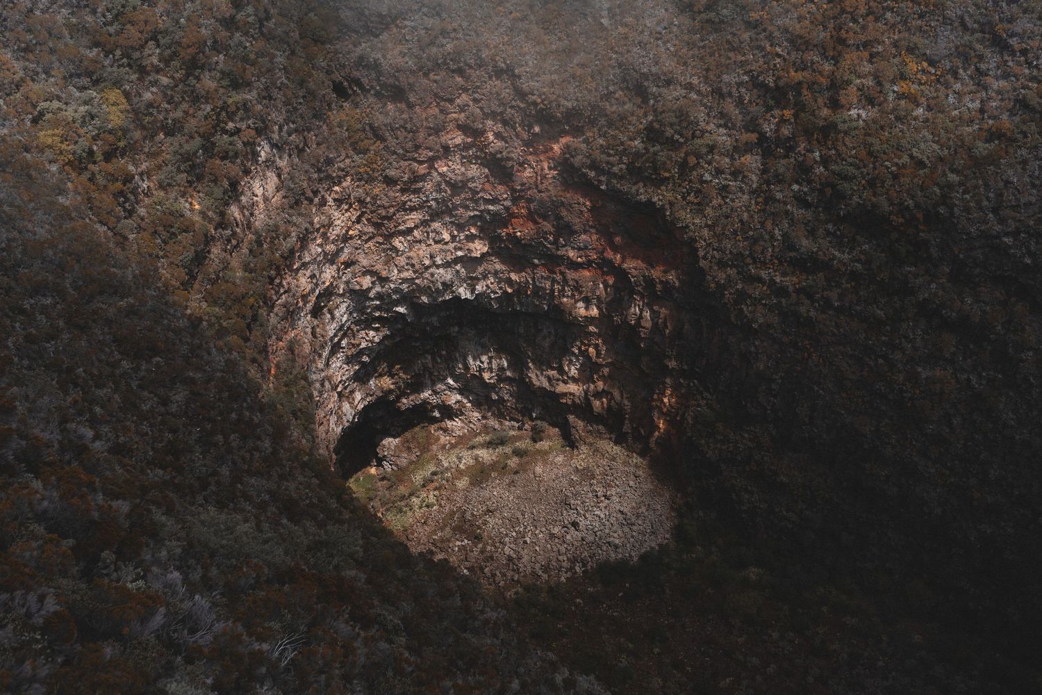 Dark rocky cave tunnel opening with rugged stone walls and dim natural light illuminating the hollow interior.