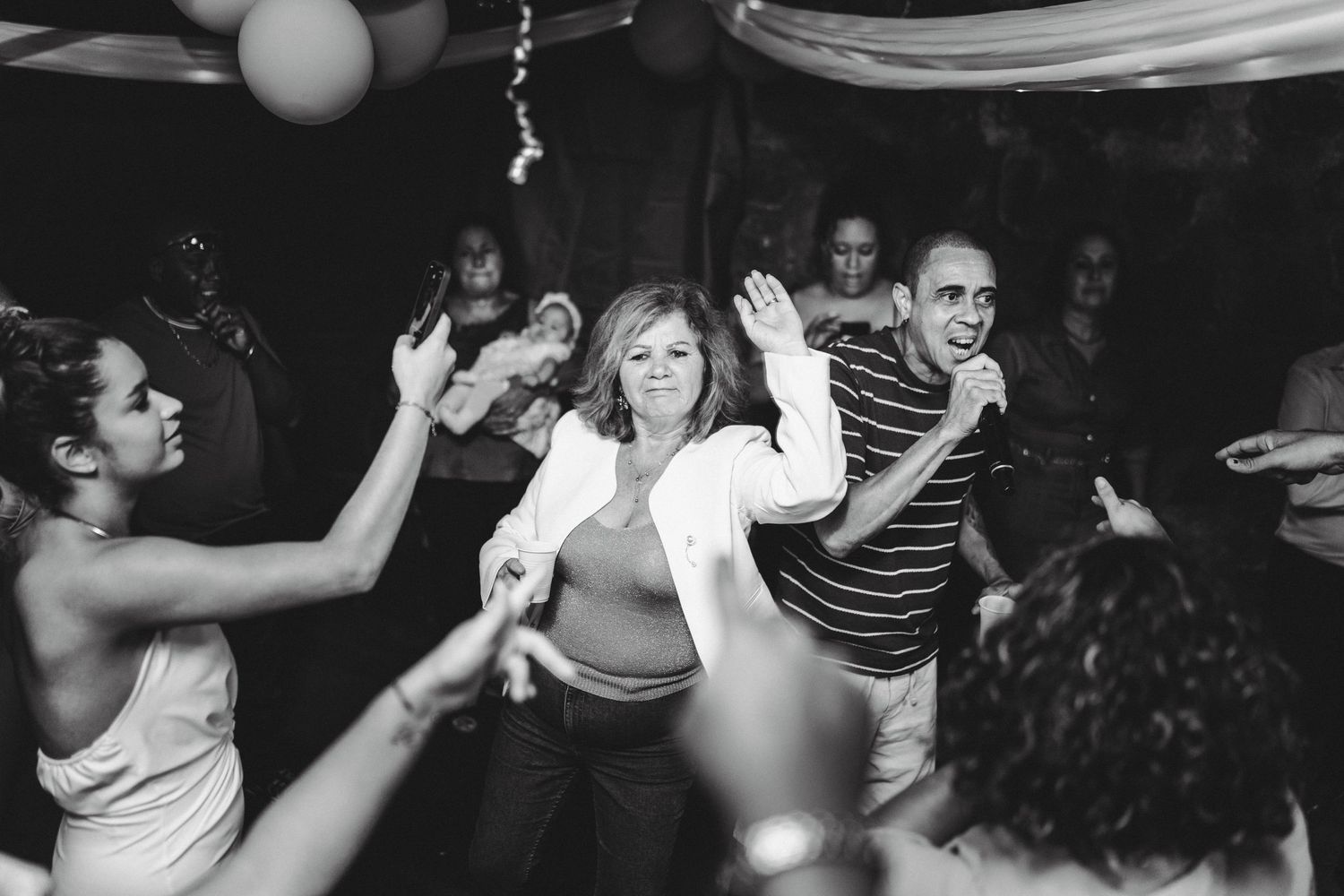 Black and white photo of people dancing and celebrating at a lively party or wedding reception.