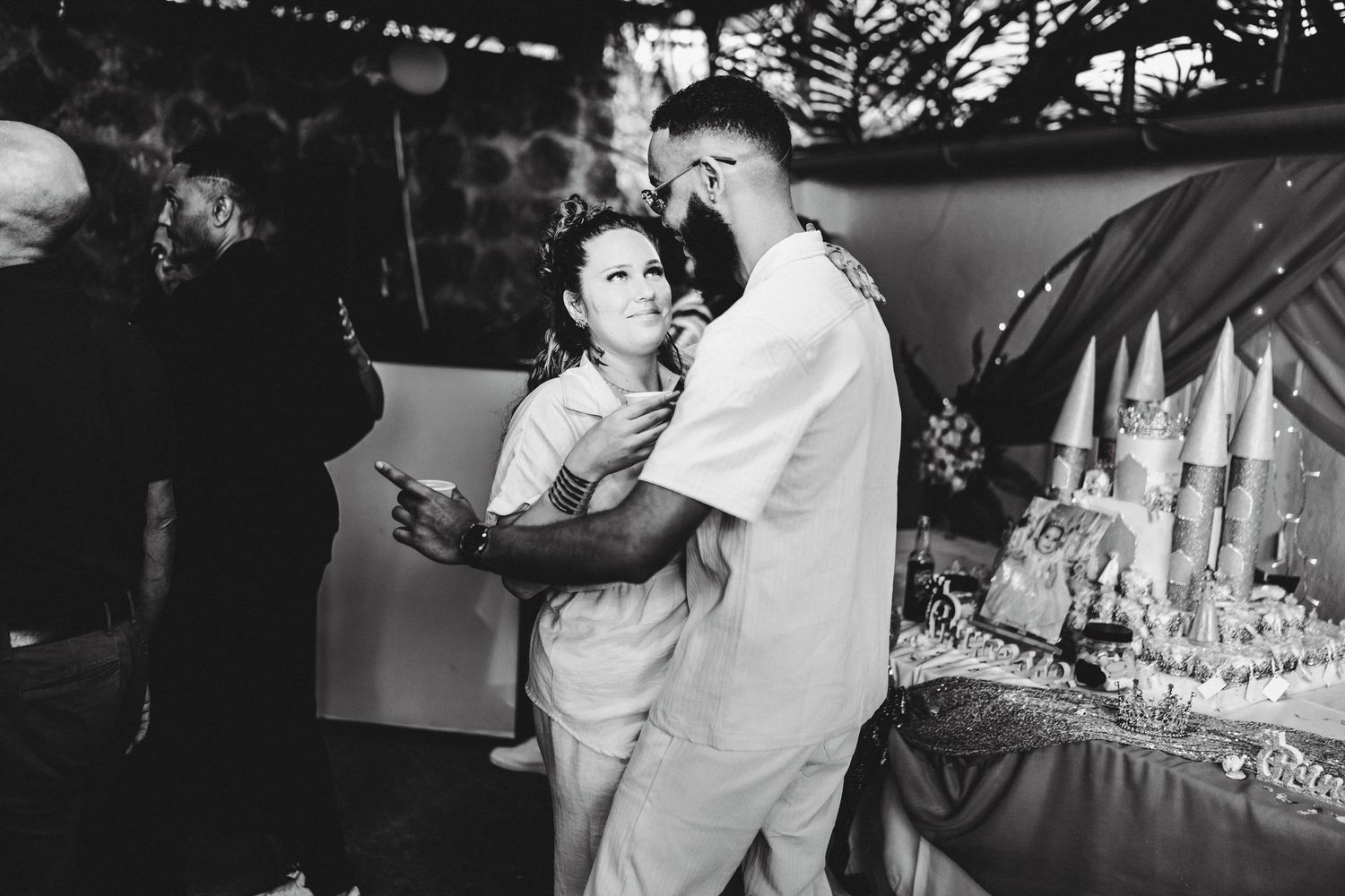 Black and white photo of a couple sharing a tender moment near a decorated wedding cake at a reception.