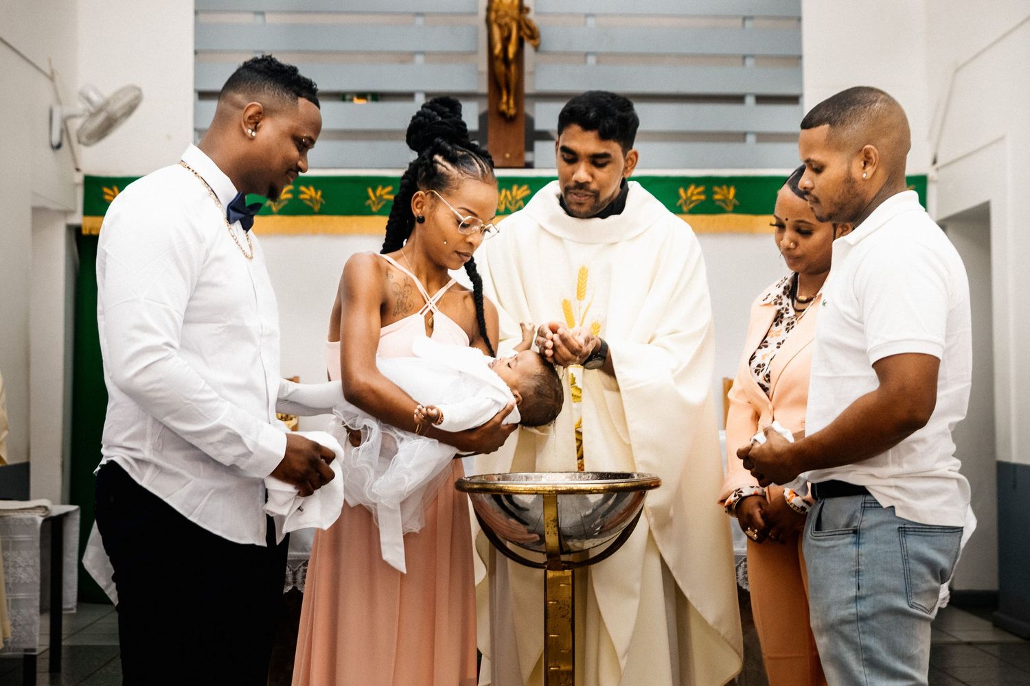 Family gathered around baptismal candle during a Catholic christening ceremony in a church.