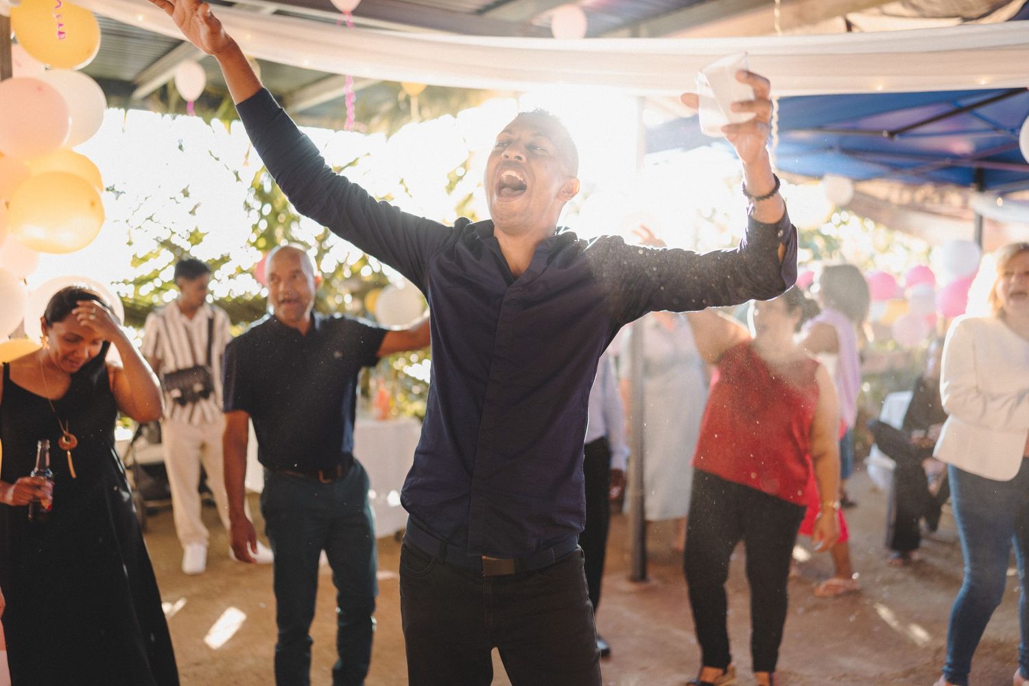 Man dancing joyfully with arms raised at an outdoor party celebration with friends.