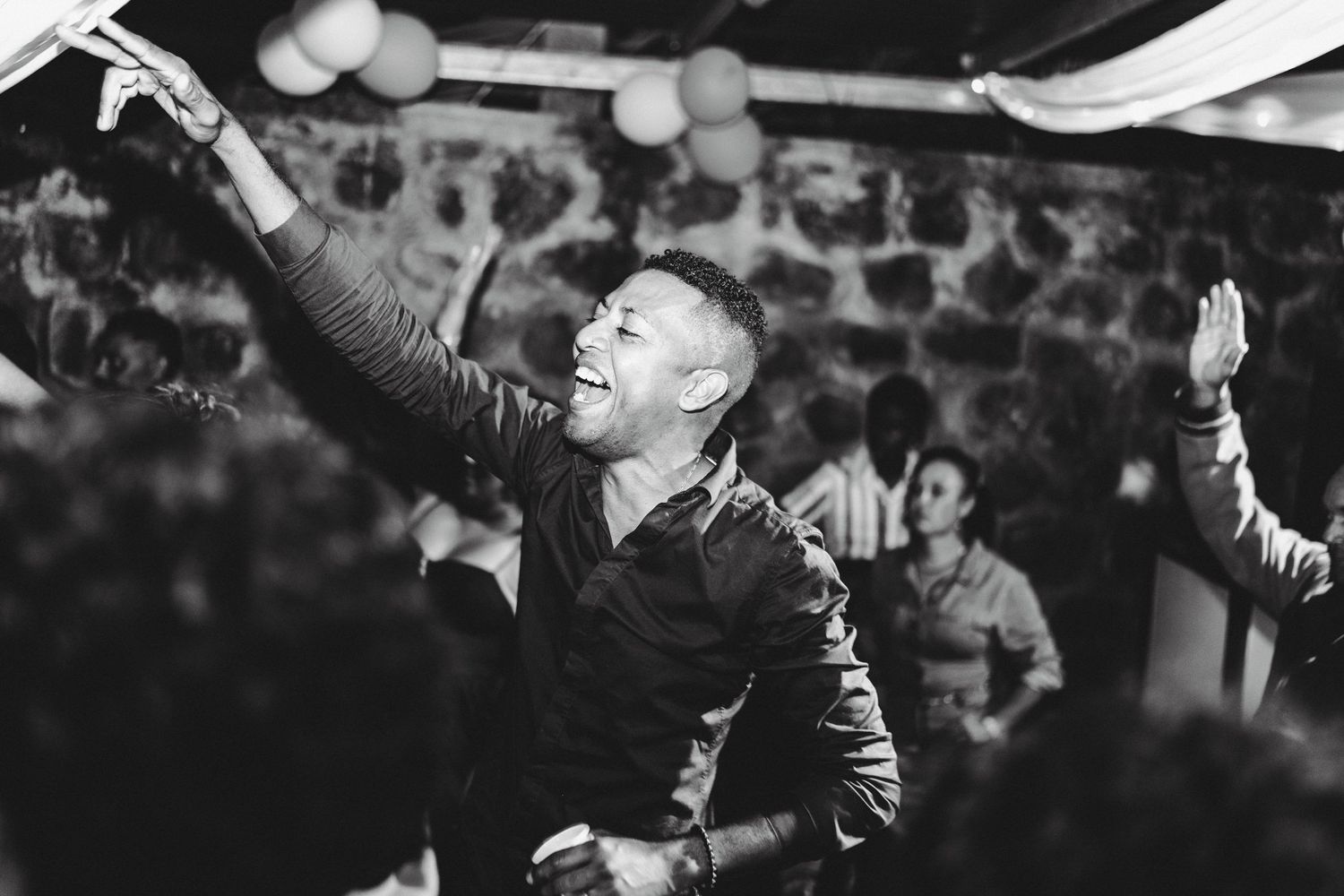 Man joyfully dancing at a lively party, arms raised, laughing, in black and white photography.