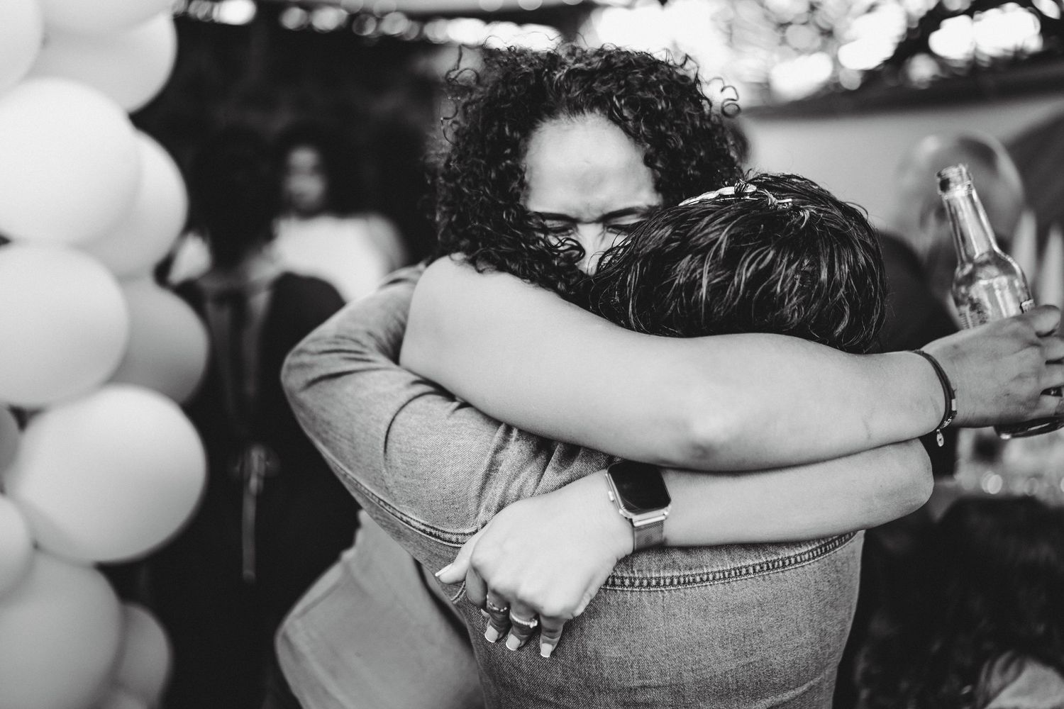 Two women share a warm embrace at a party with balloons in black and white photo.