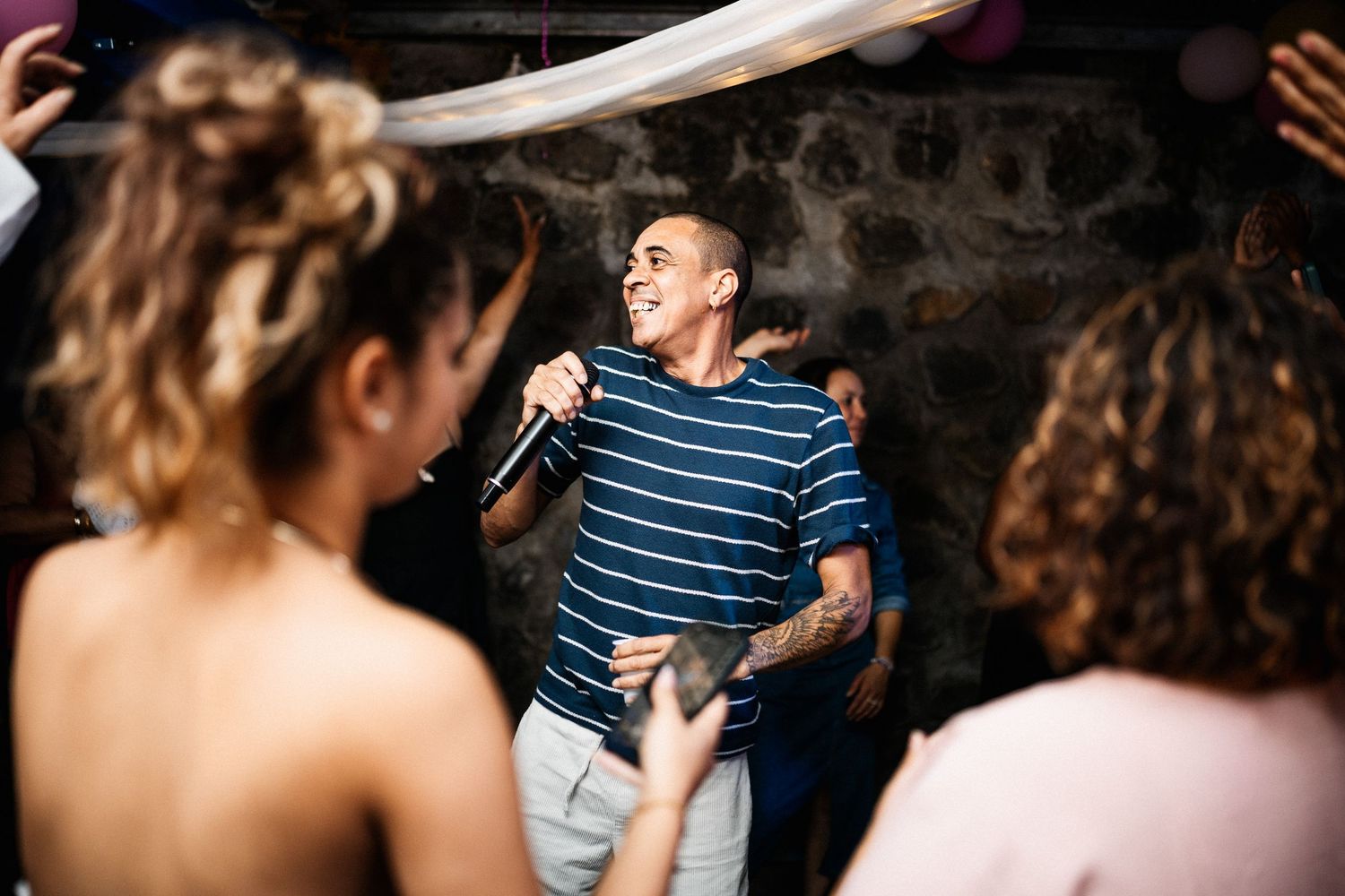 Smiling man in striped shirt singing into microphone while entertaining guests at a lively party.