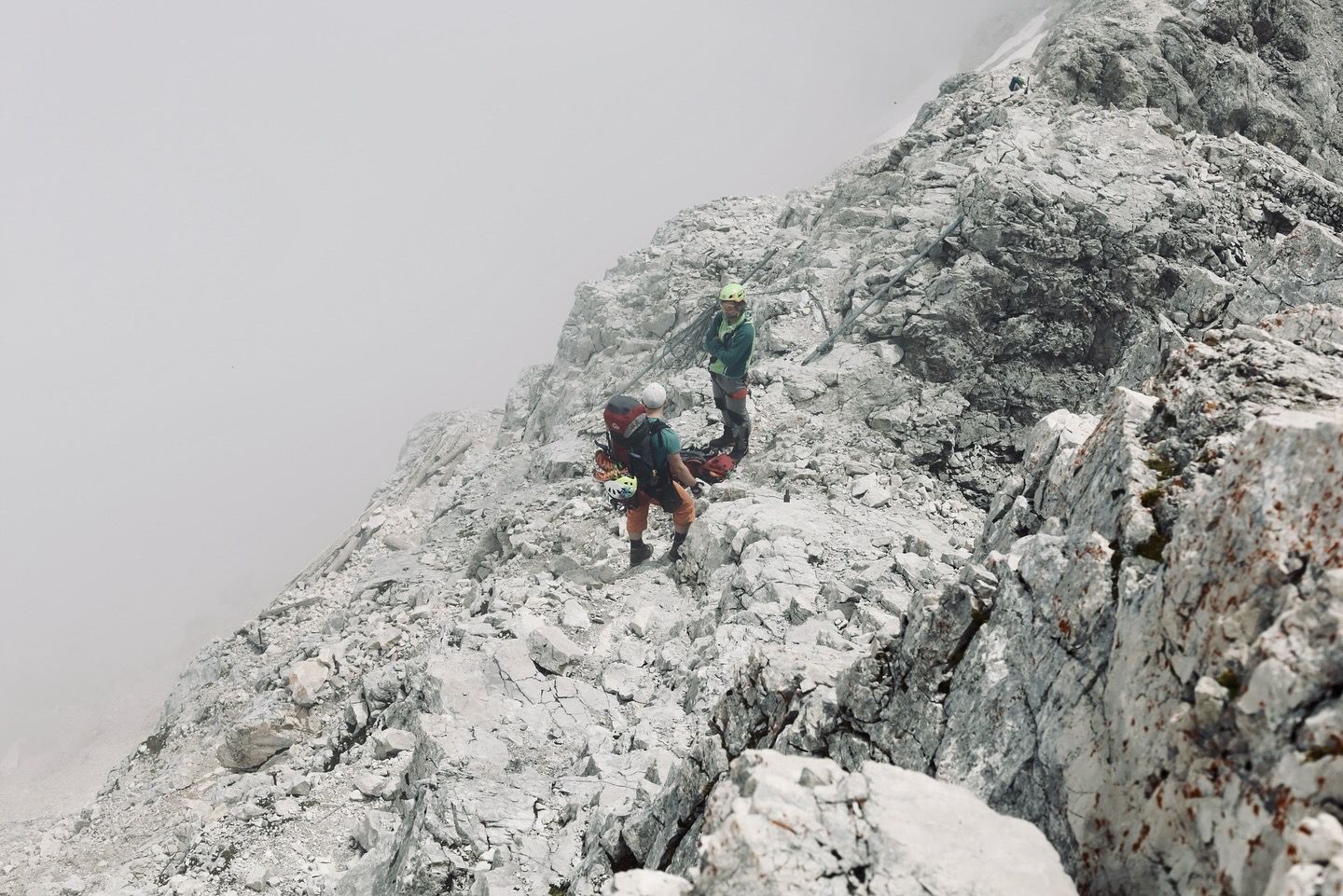 Two mountaineers climbing a rocky ridge in foggy alpine conditions.